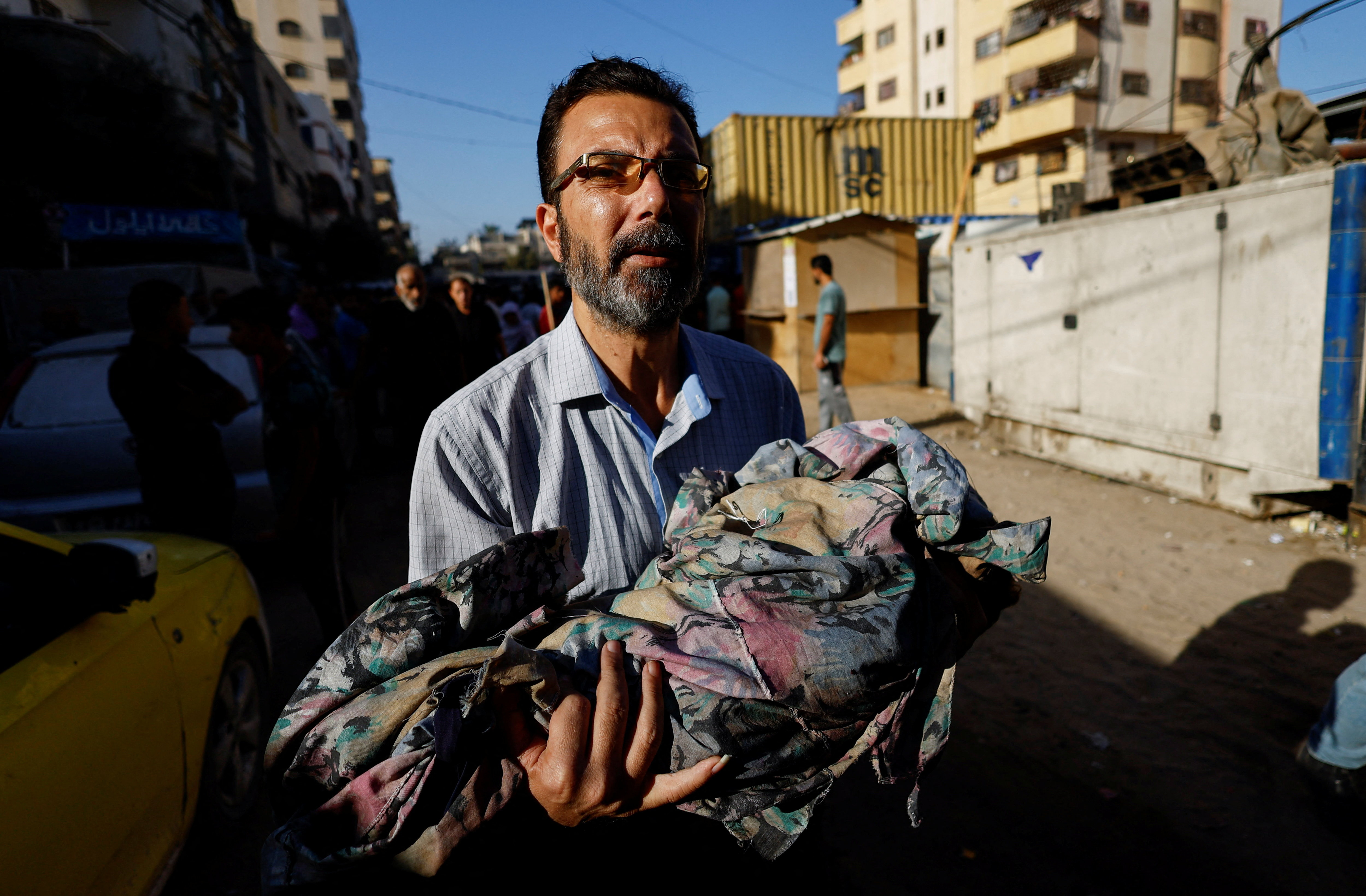 A man carries the body of Palestinian child killed in Sunday's Israeli strikes, according to medics, during the funeral at al-Awda Hospital in the central Gaza Strip, October 20, 2025.