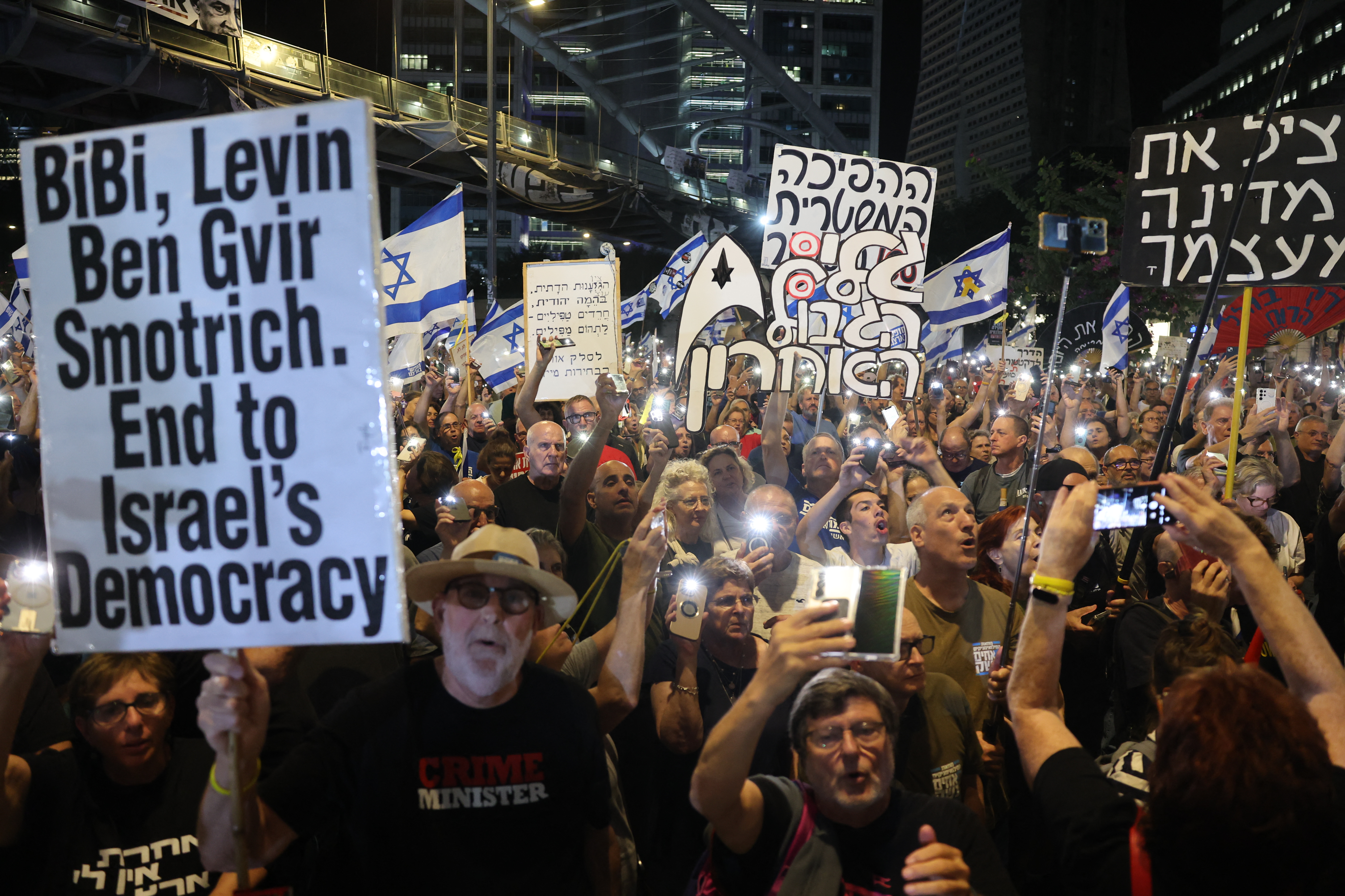 Israeli anti-government protesters lift placards and flags