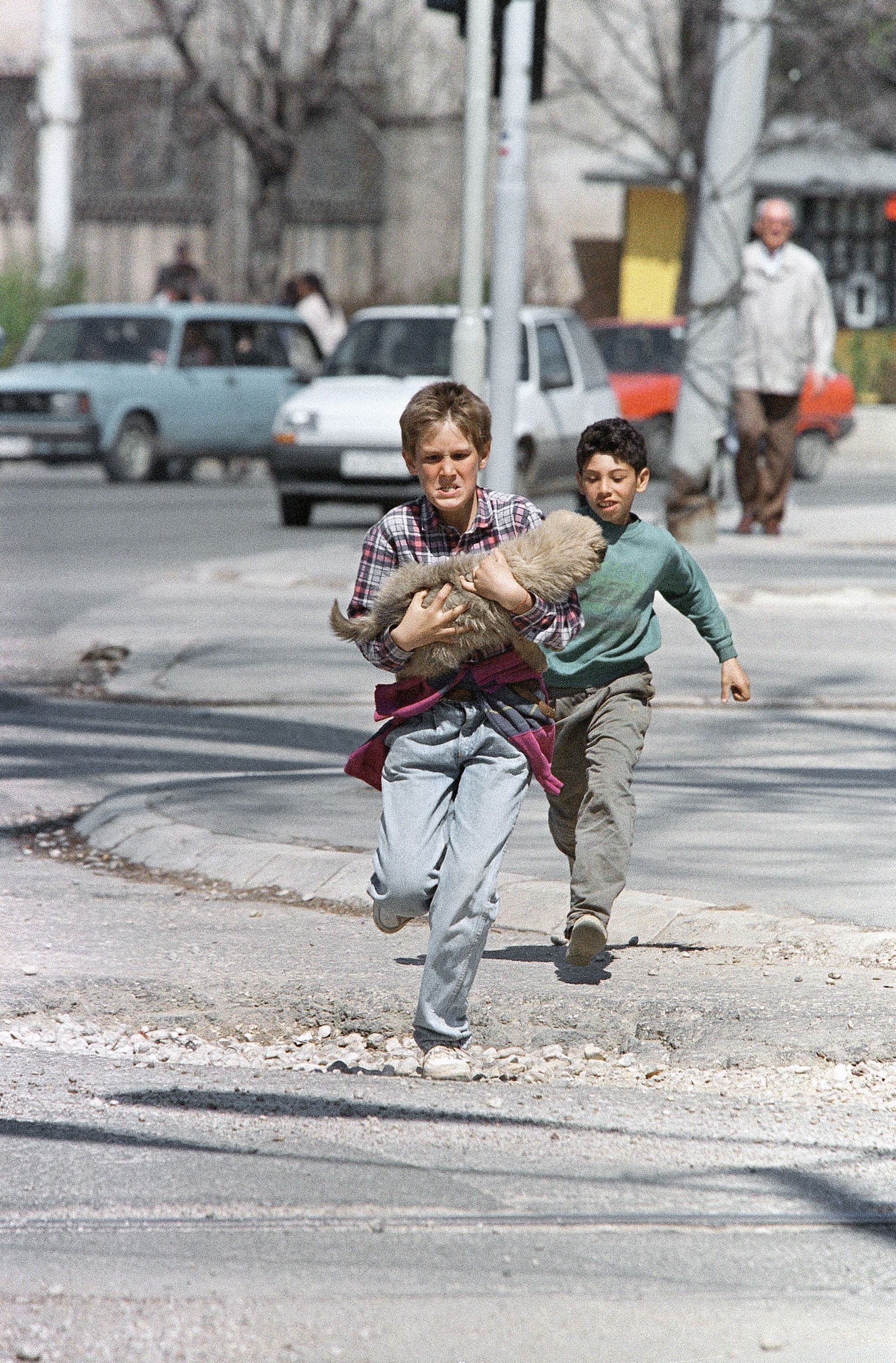 Carrying his dog, a boy sprints across a central intersection, which is sometimes targeted by snipers, on Thursday, April 20, 1995, in Sarajevo