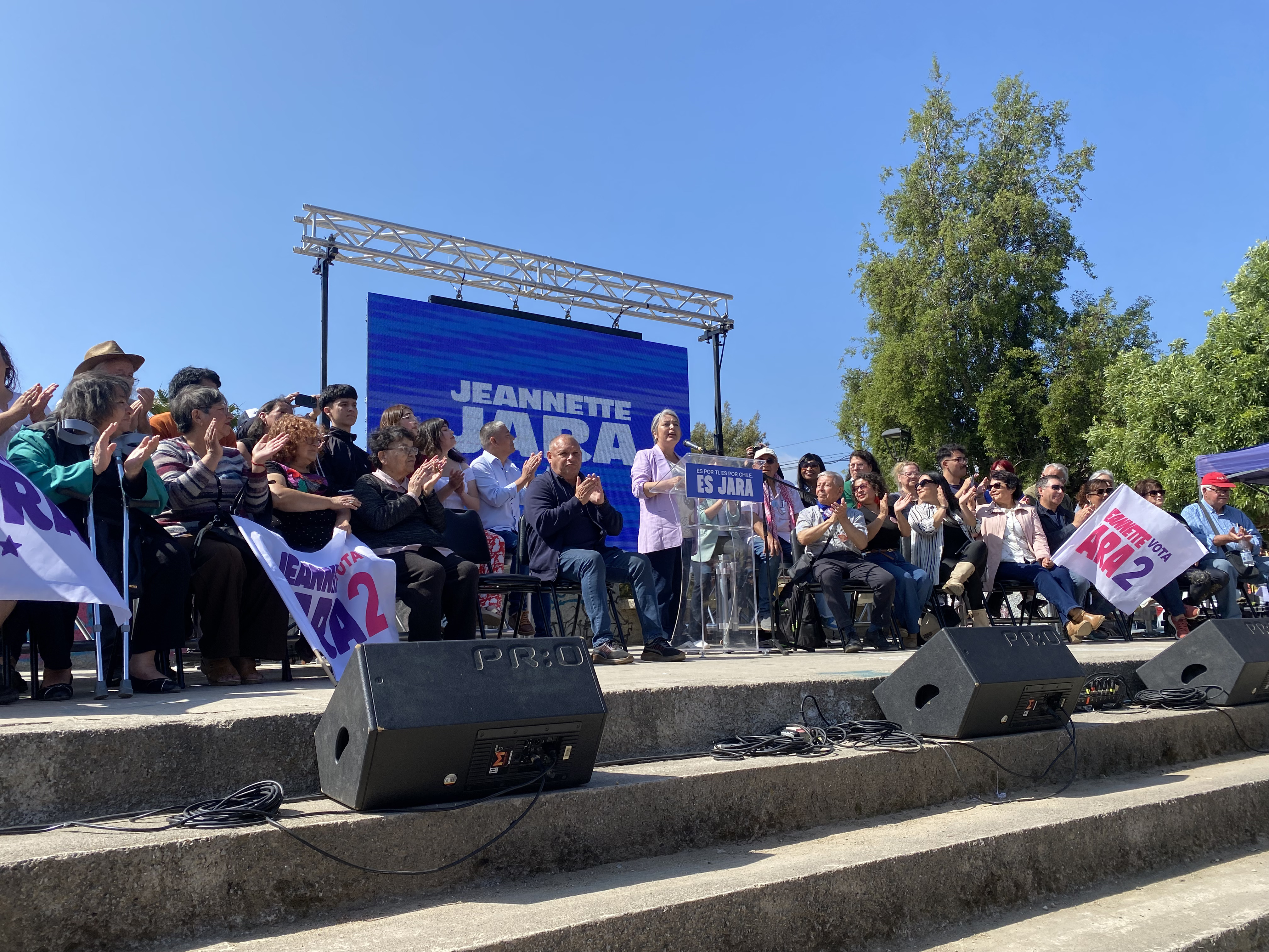 A rally for Jeannette Jara, with the candidate speaking at an outdoor podium.