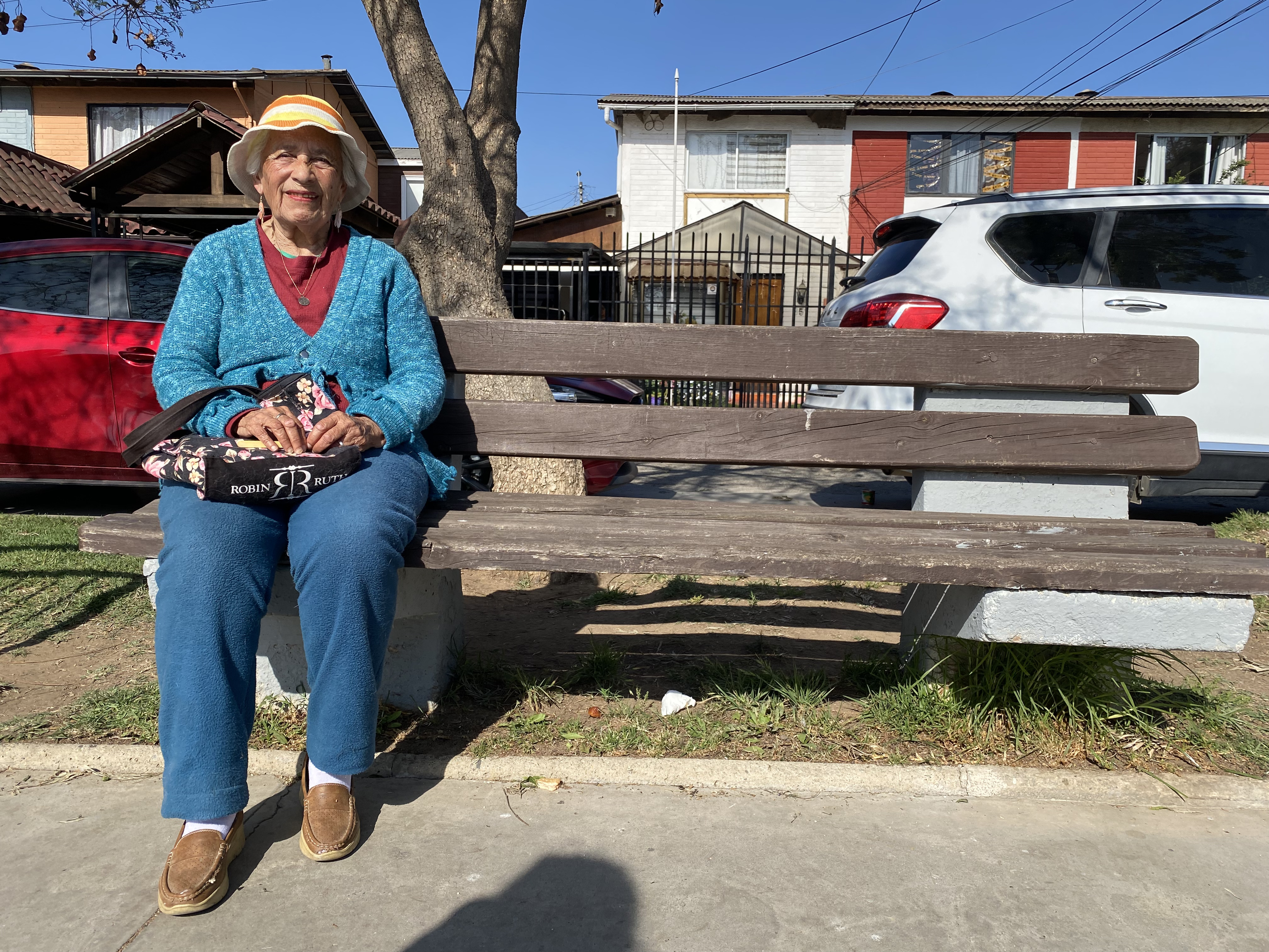 A retired woman sits on a park bench.