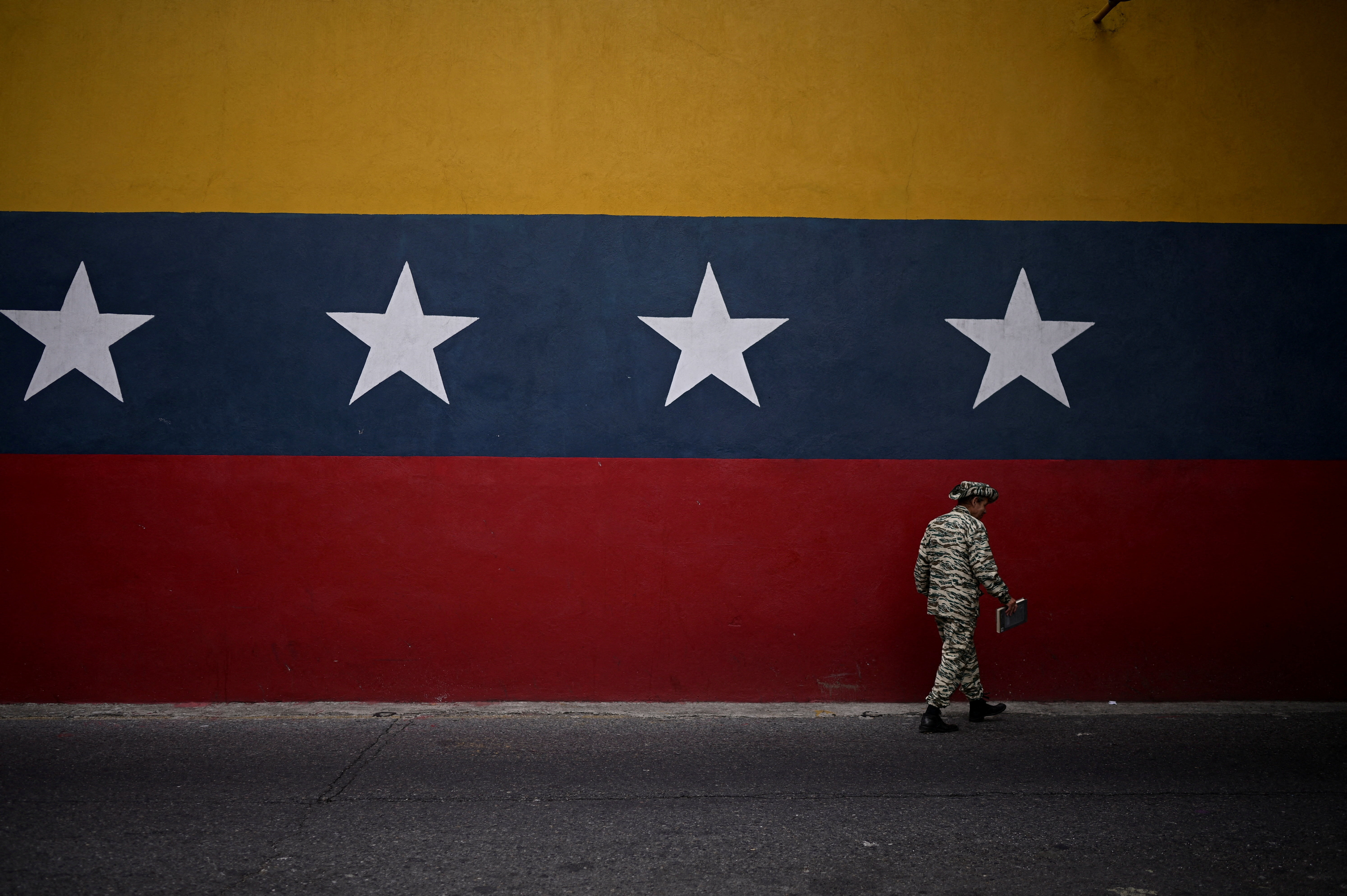 A member of the Bolivarian Militia walks past a mural with the colors of the Venezuelan flag