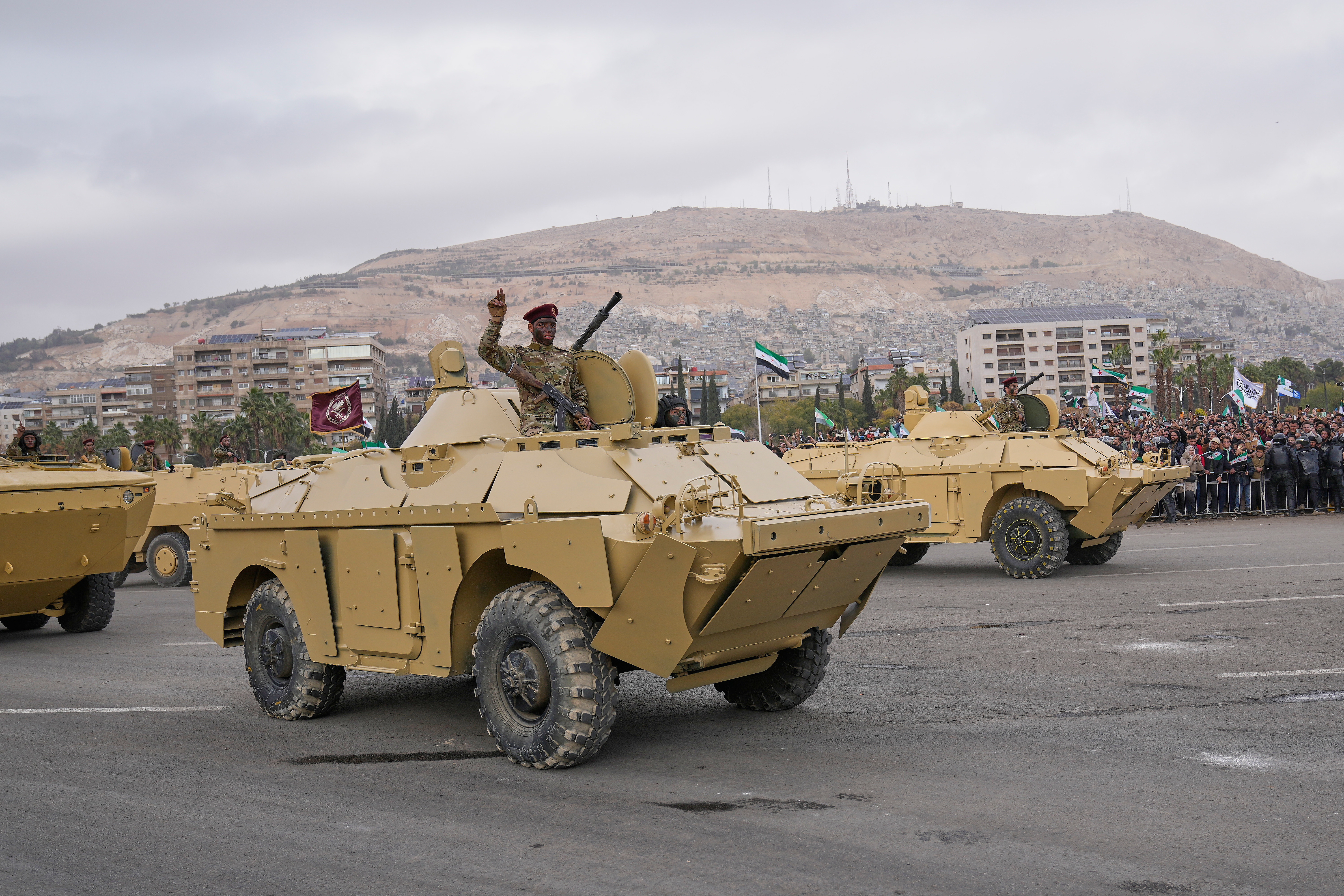 Syrian army soldiers stand on their armoured personnel carriers during a parade