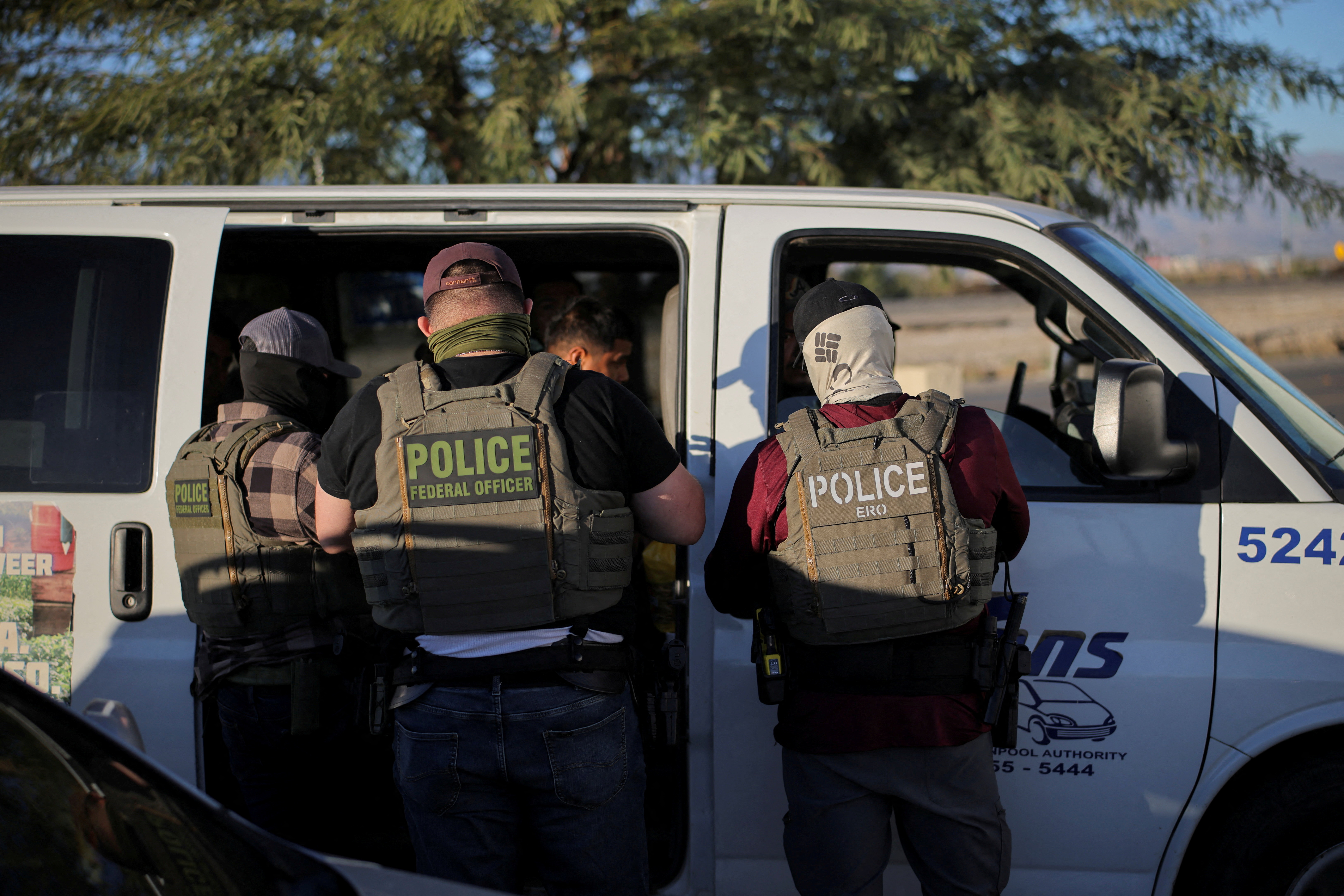 FILE PHOTO: Immigration and Customs Enforcement (ICE) agents check the identity documents of a group of agricultural workers at a grocery store parking lot during an immigration raid in Mecca, California, U.S. December 19, 2025. REUTERS/Daniel Cole/File Photo