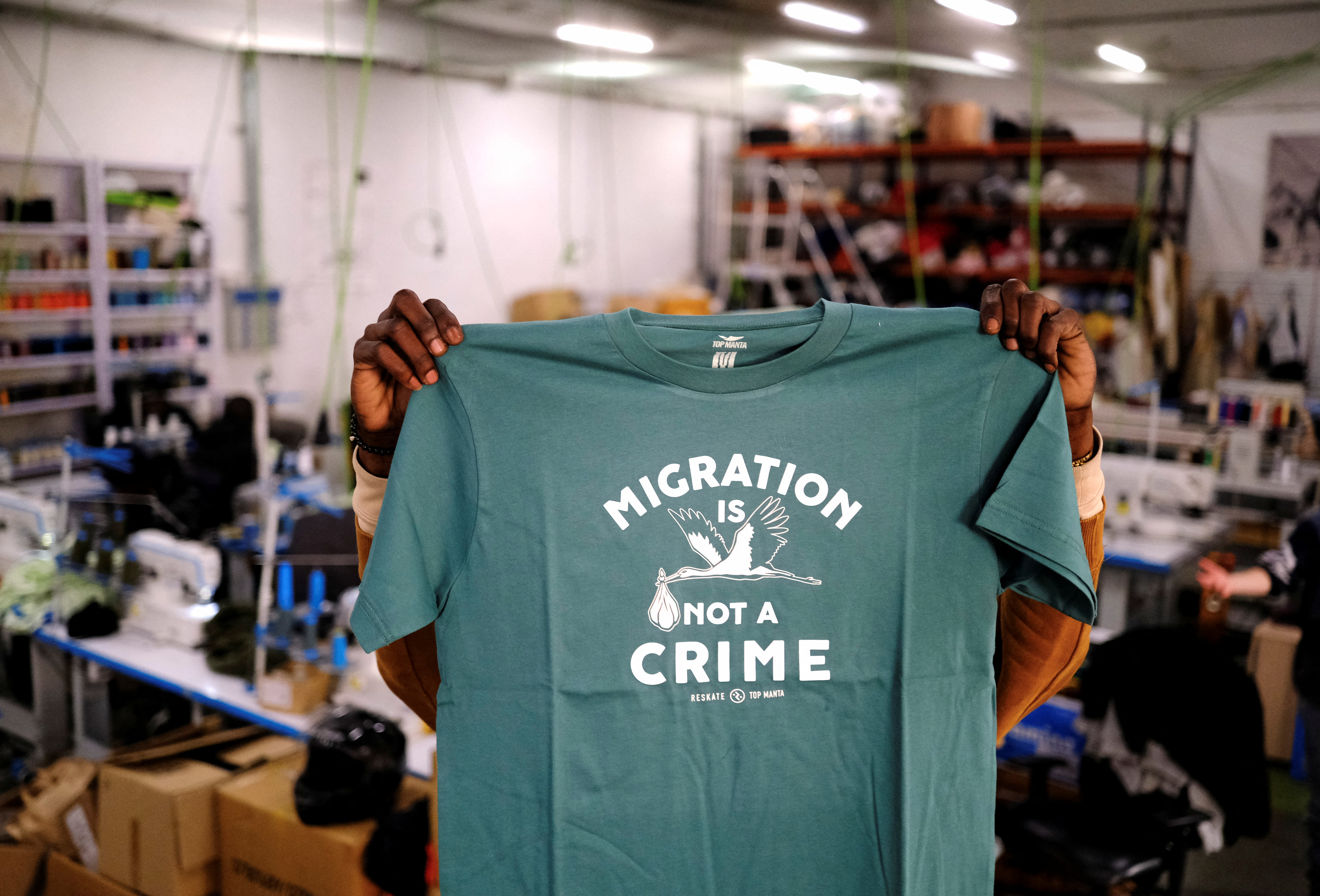 A person holds up a T-shirt with "Migration is not a crime" printed on it.
