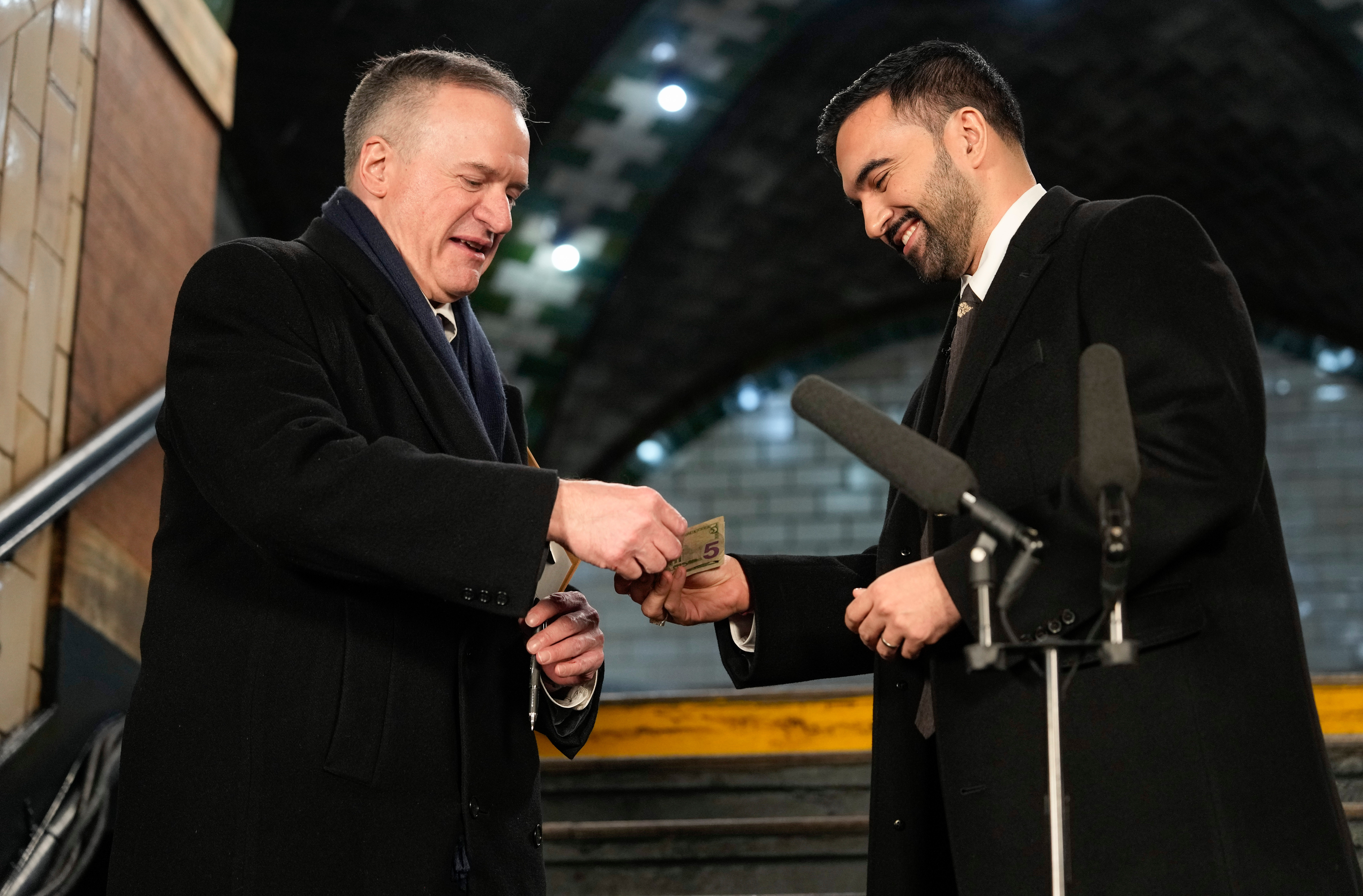 Mamdani, right, hands nine dollars to city clerk Michael McSweeney before signing a registry