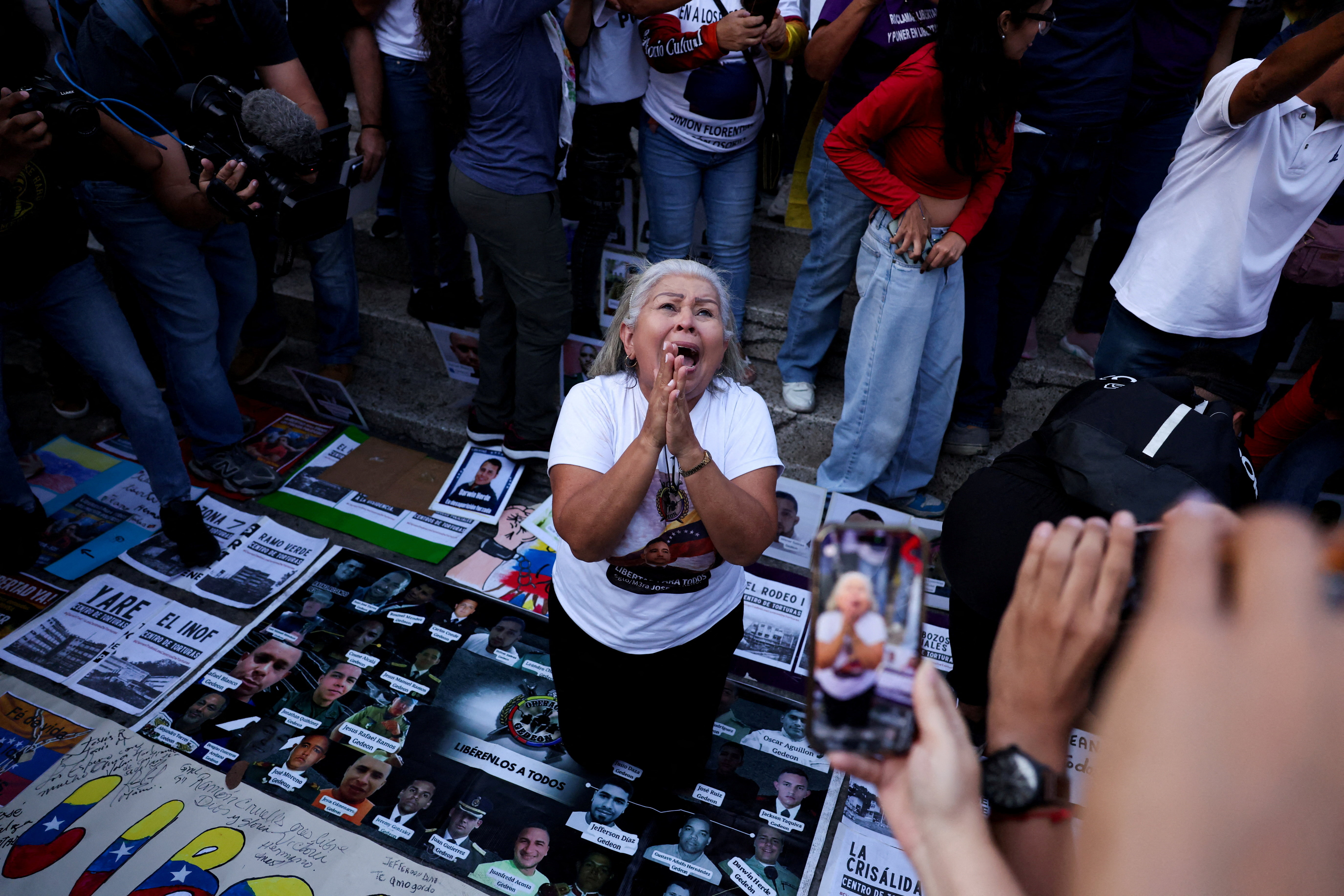 A woman kneels and clasps her hands in prayer atop a pile of posters calling for the release of political prisoners
