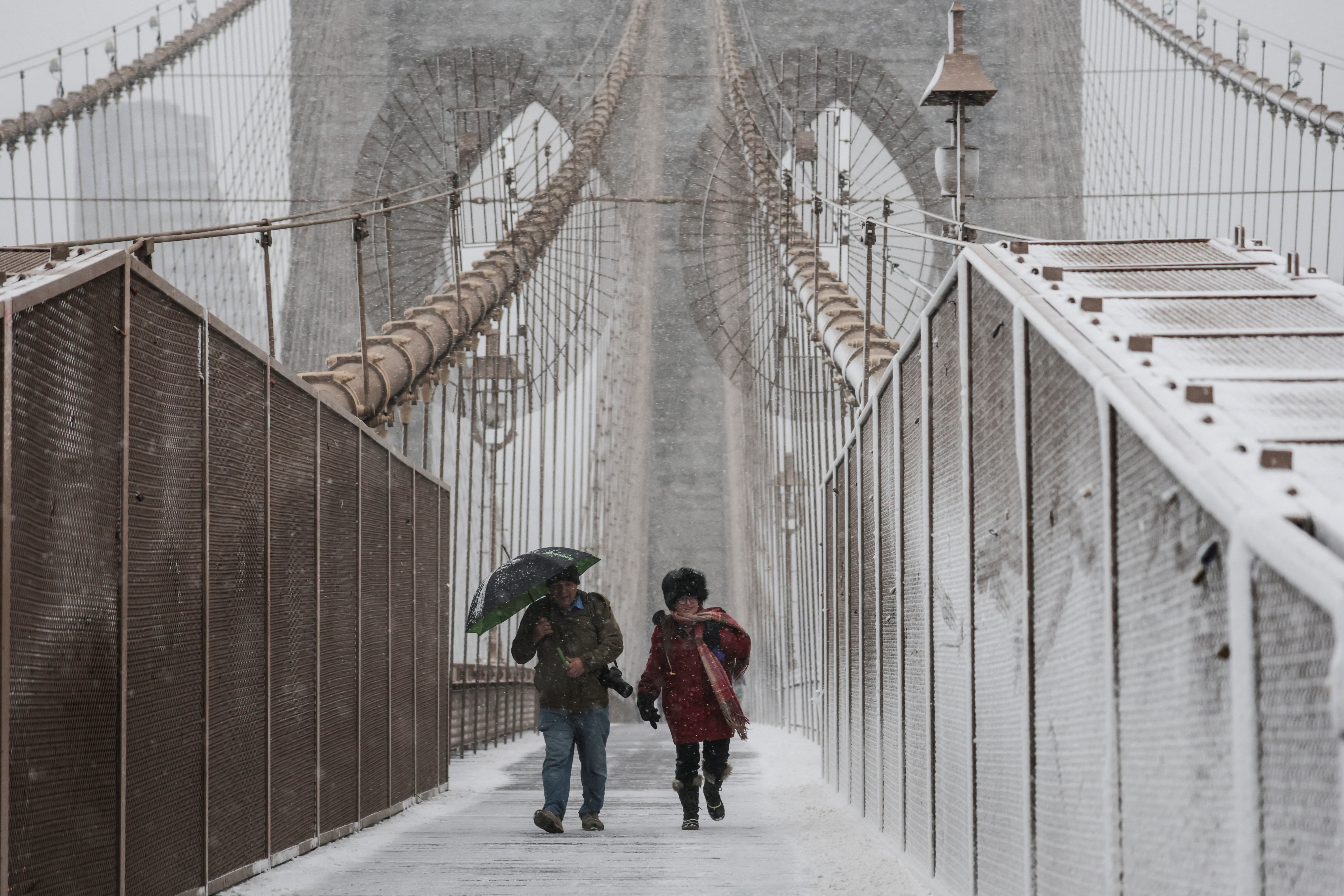 People walk across the Brooklyn Bridge as snow falls during a winter storm in New York