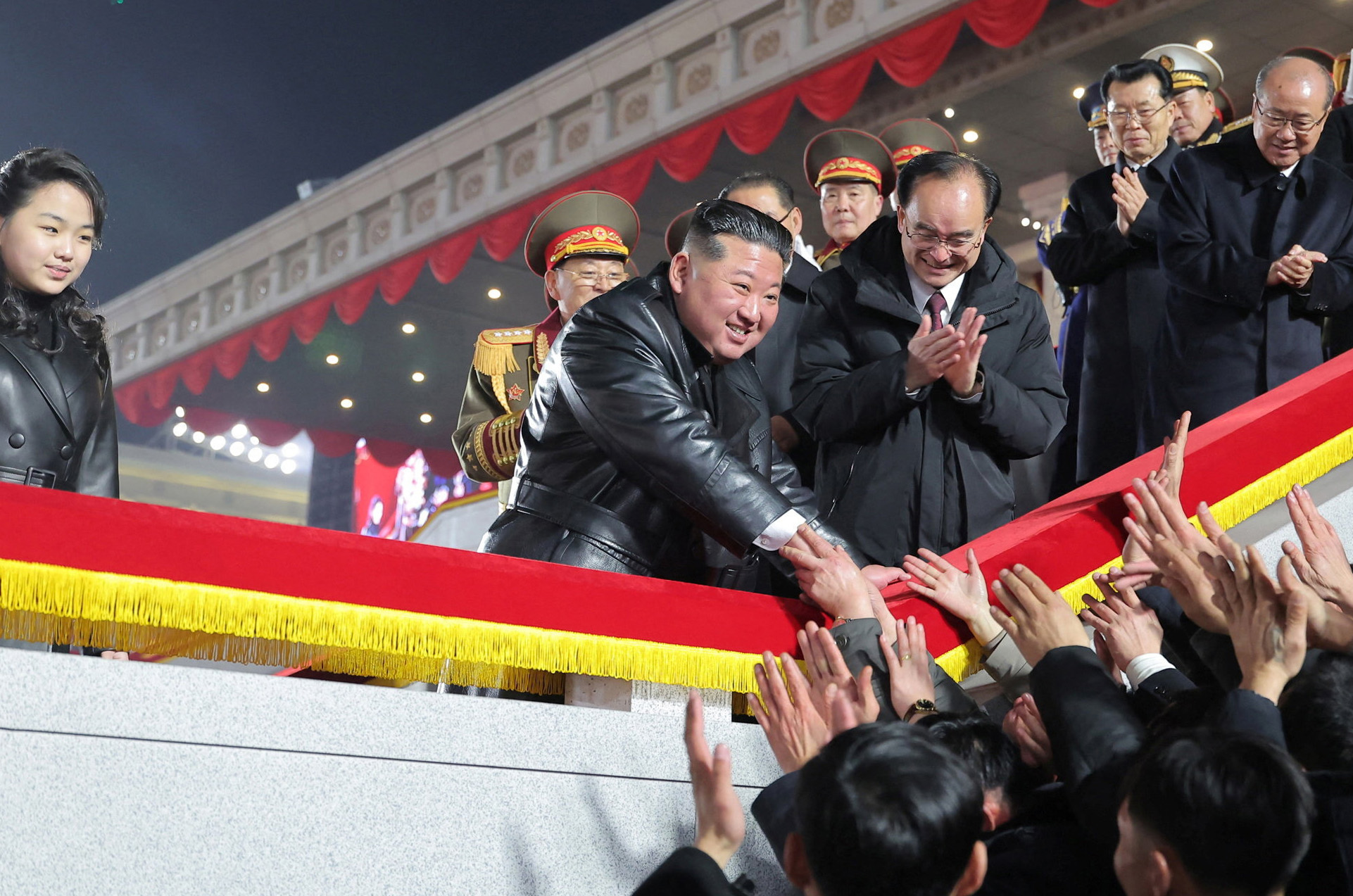 North Korean leader Kim Jong Un greets attendees as his daughter Kim Ju Ae watches during a military parade
