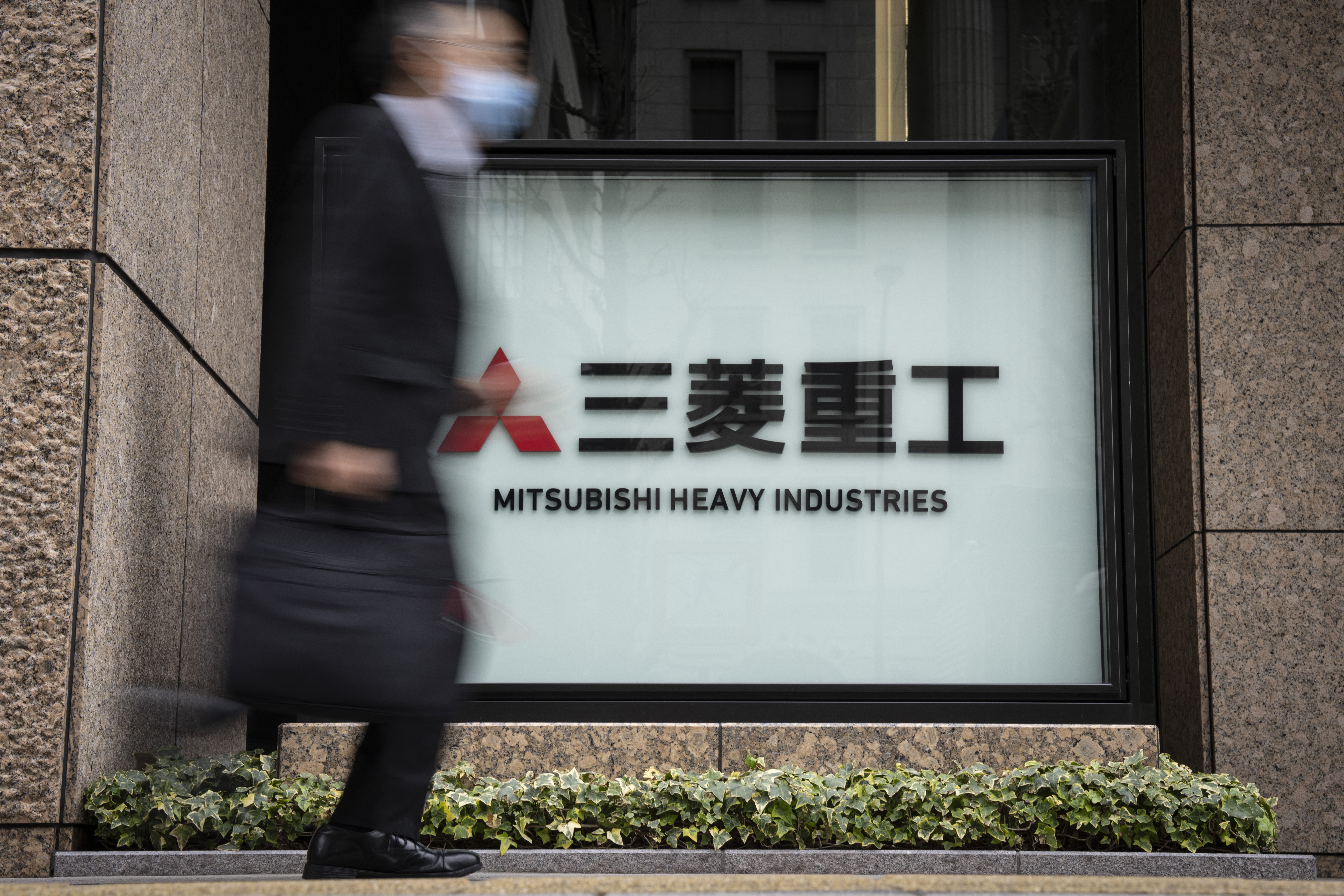 A man walks past a Mitsubishi Heavy Industries (MHI) logo outside the companys headquarters in Tokyo on February 24, 2026. China's commerce ministry took action against 40 Japanese companies and entities on February 24, 2026, citing national security concerns over their military ties. (Photo by Yuichi YAMAZAKI / AFP)