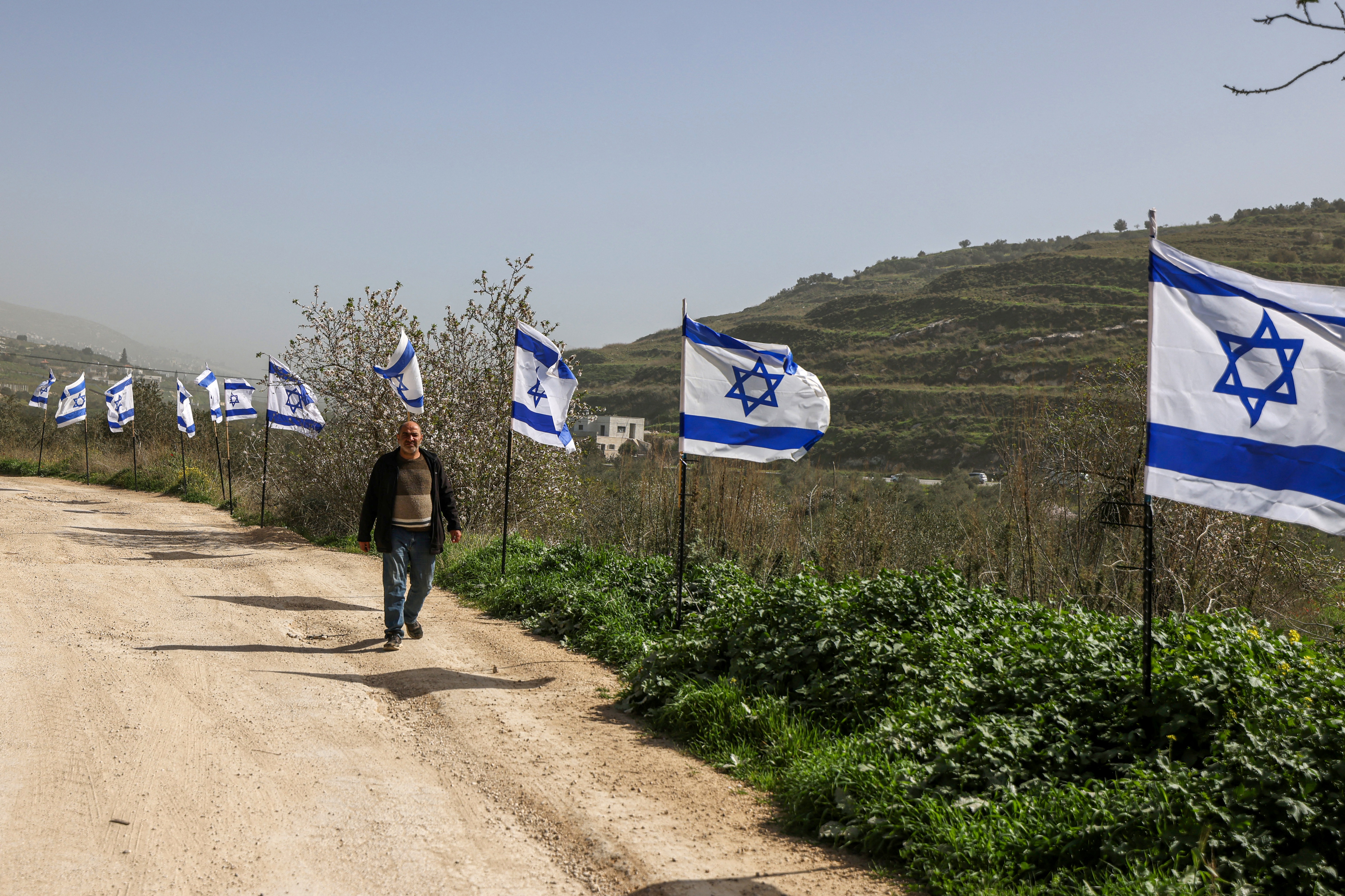A Palestinian man walks past a fence decorated with Israeli flags installed by Jewish settlers