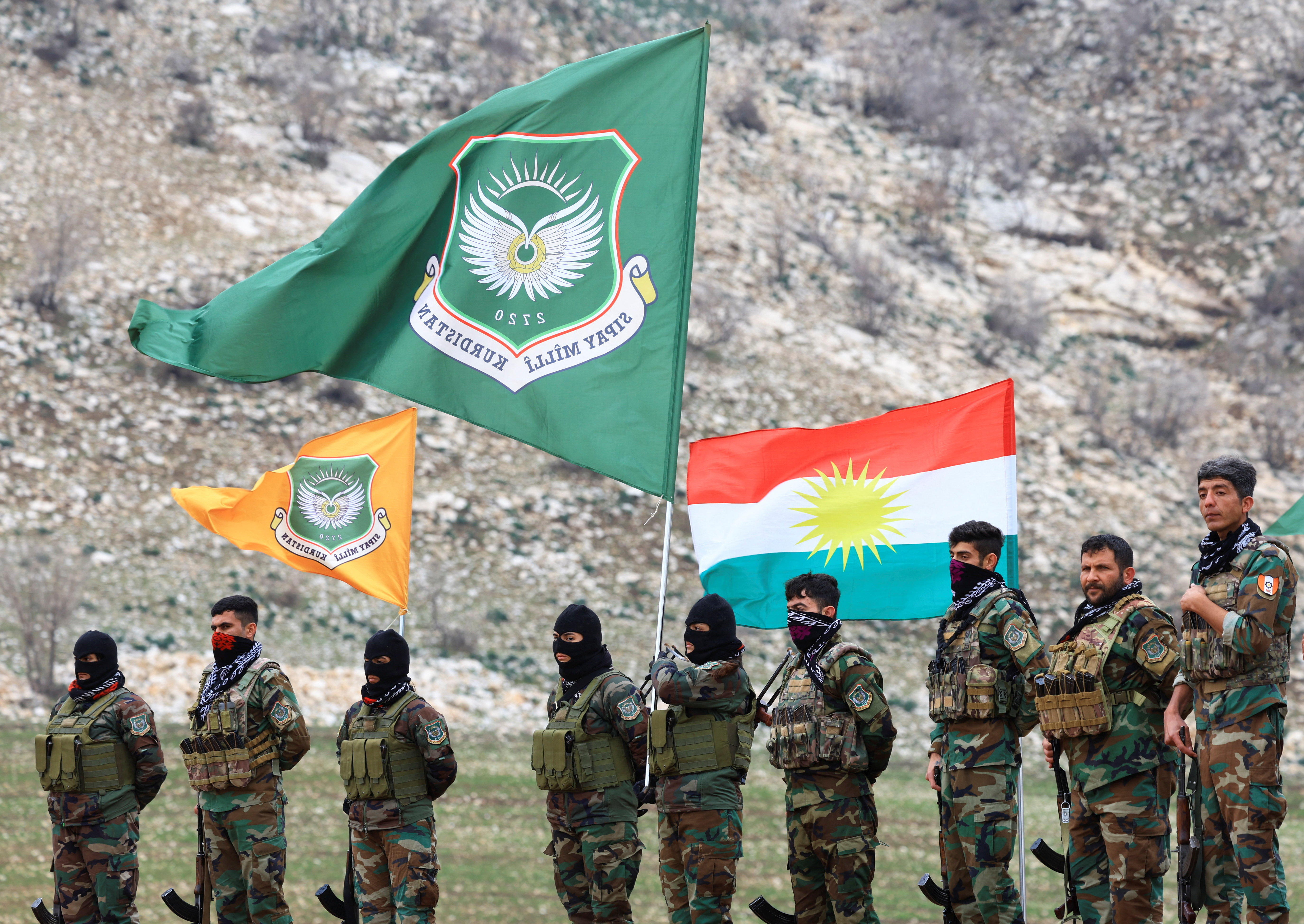 Kurdish fighters stand in front of flags