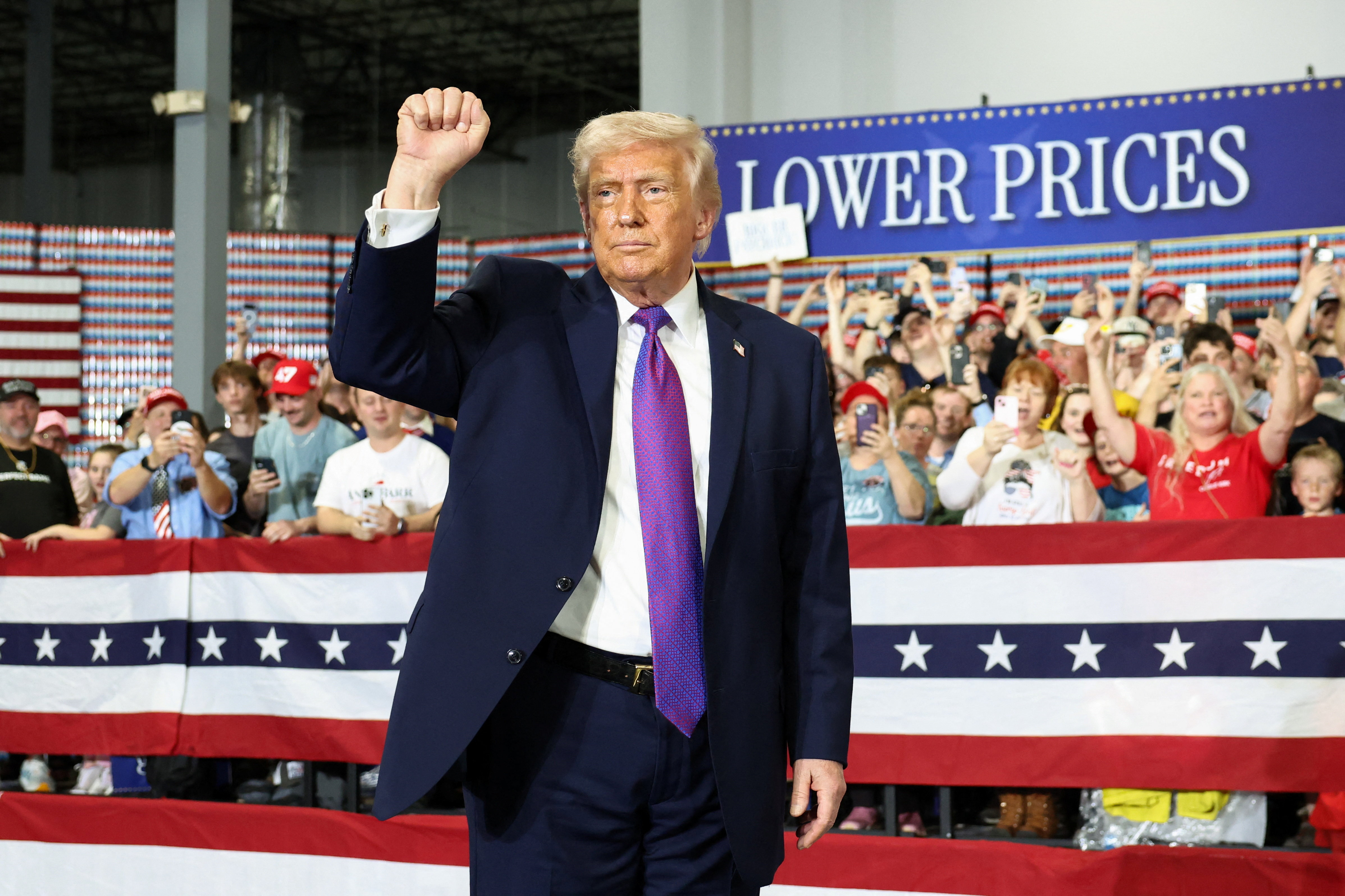 Trump rallies in front of a sign that reads, "Lower Prices"