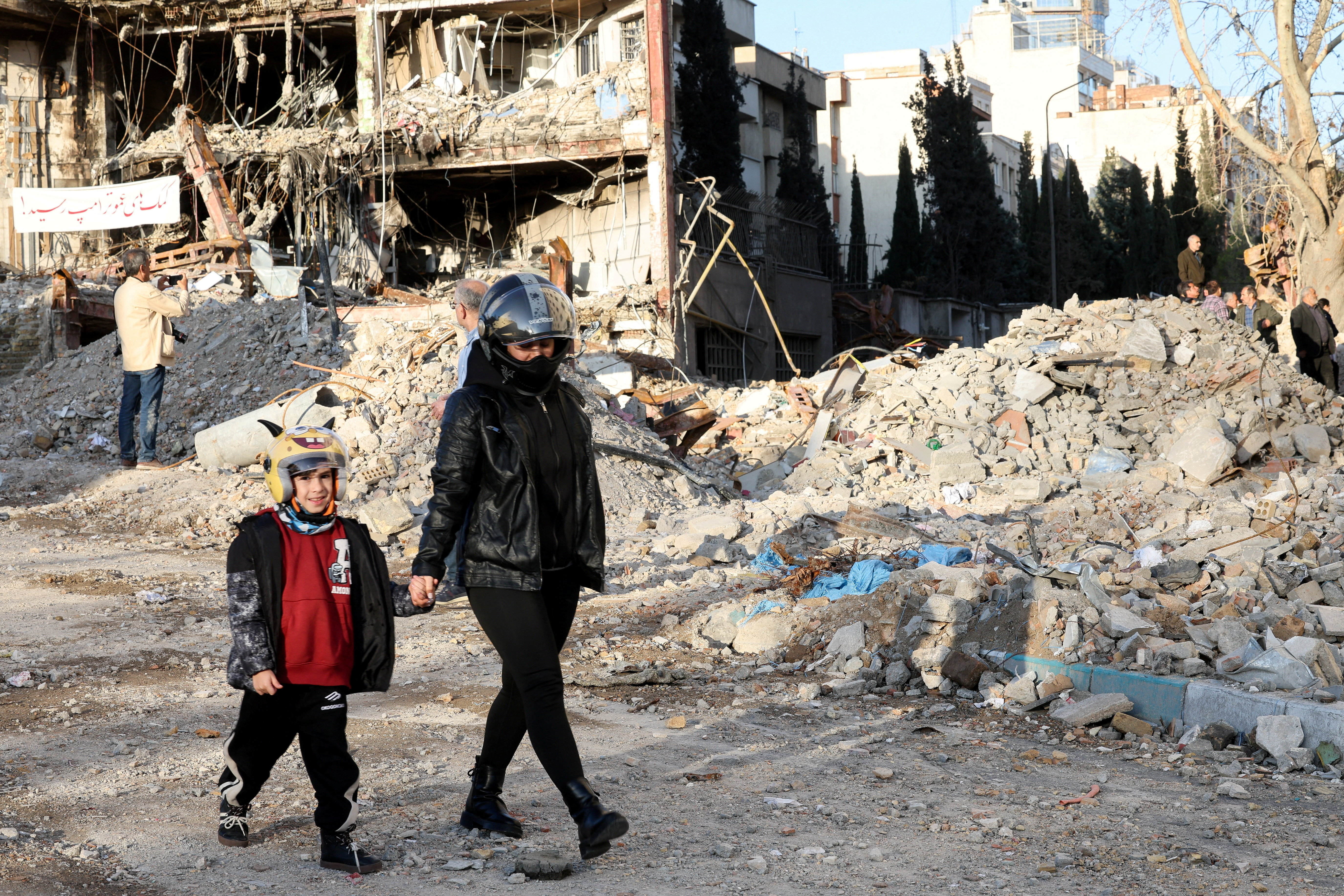 A mother and son walk near a building destroyed in a strike, amid the U.S.-Israeli conflict with Iran, in Tehran