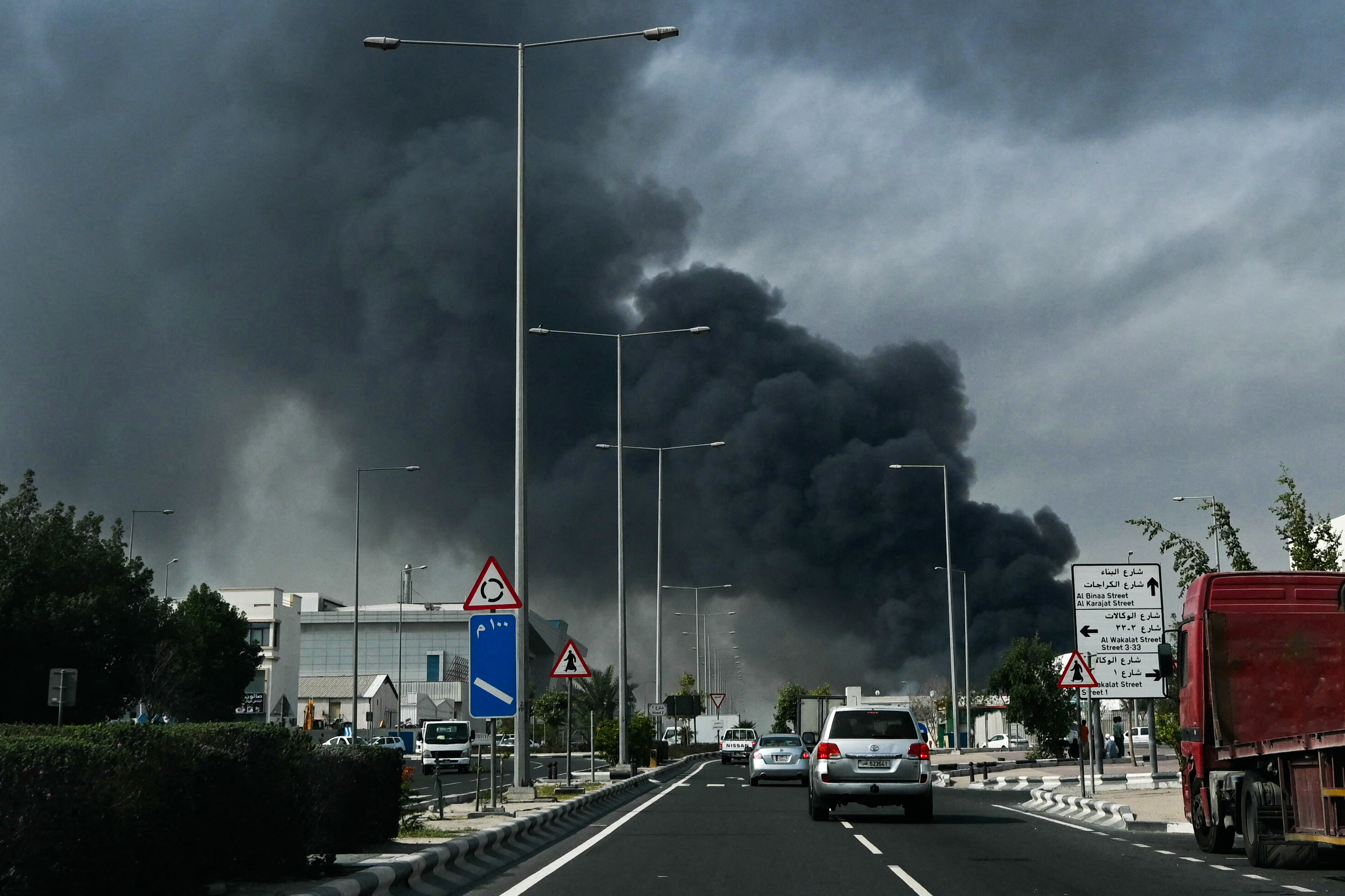 Motorists drive past a plume of smoke rising from a reported Iranian