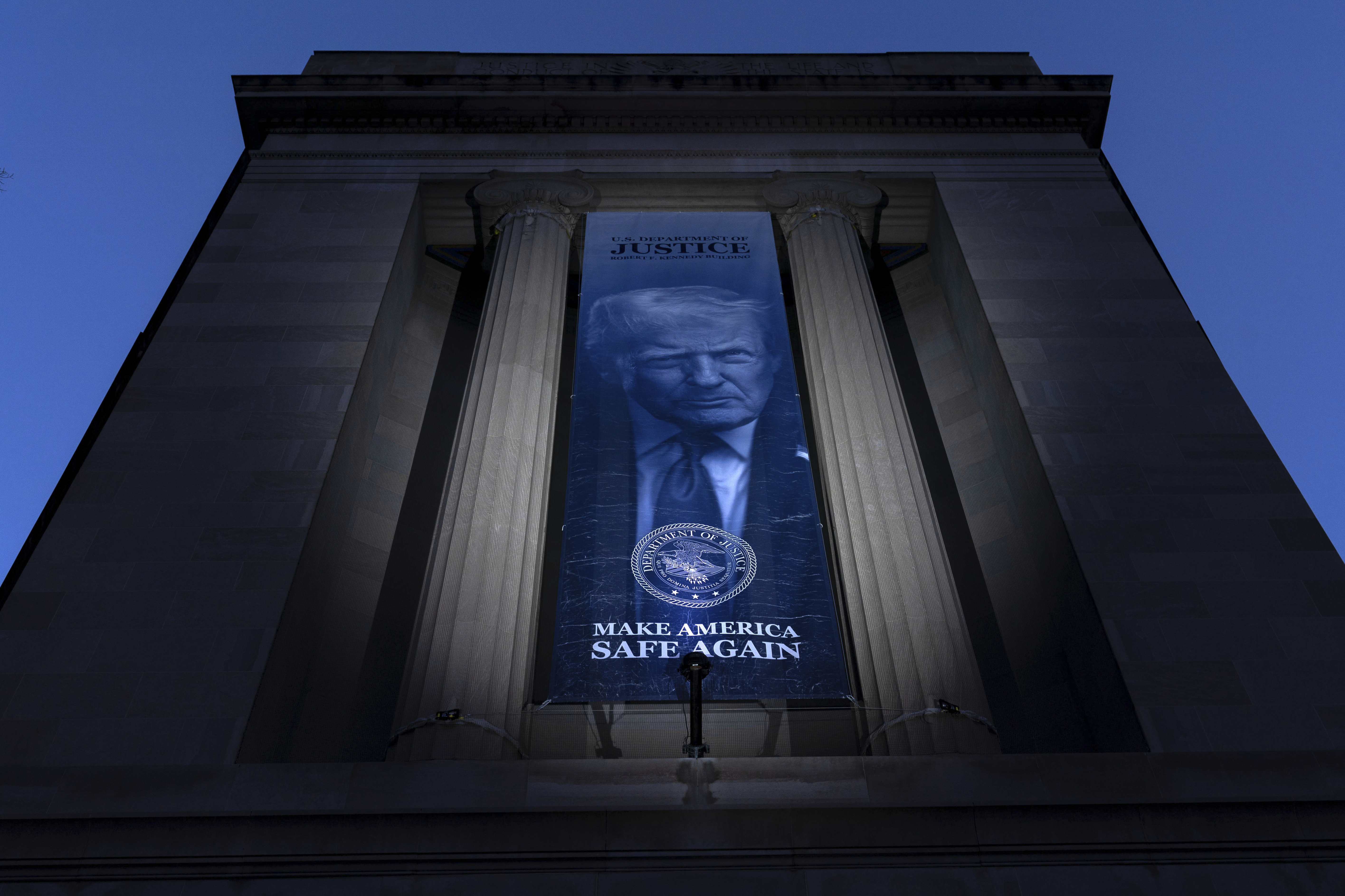 A banner of Trump hangs outside the Justice Department at night