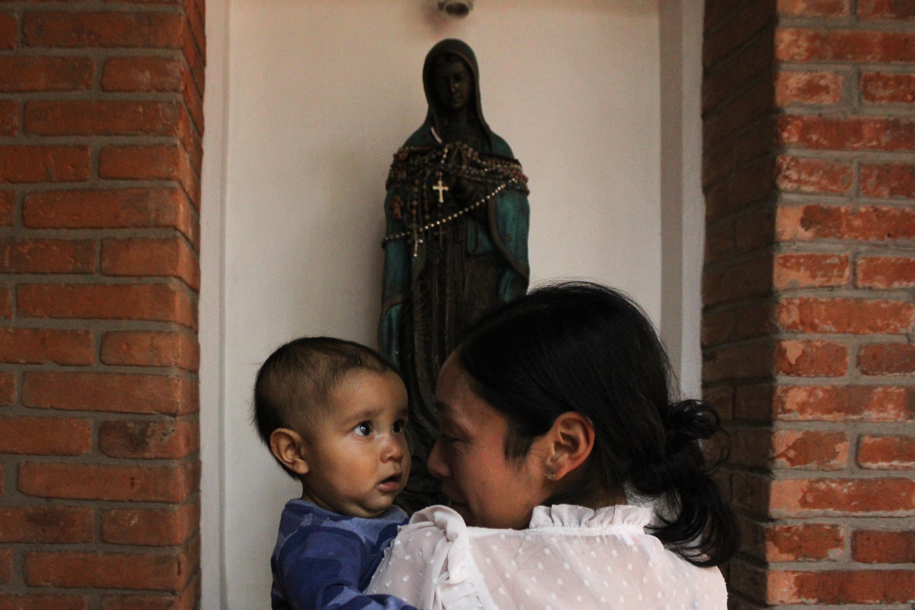 Holding Juan de Jesús before a statue of the Virgin Mary at the centre of the shelter, Luisa studies her son’s eyes, her face close to his [Mark Viales/Al Jazeera]