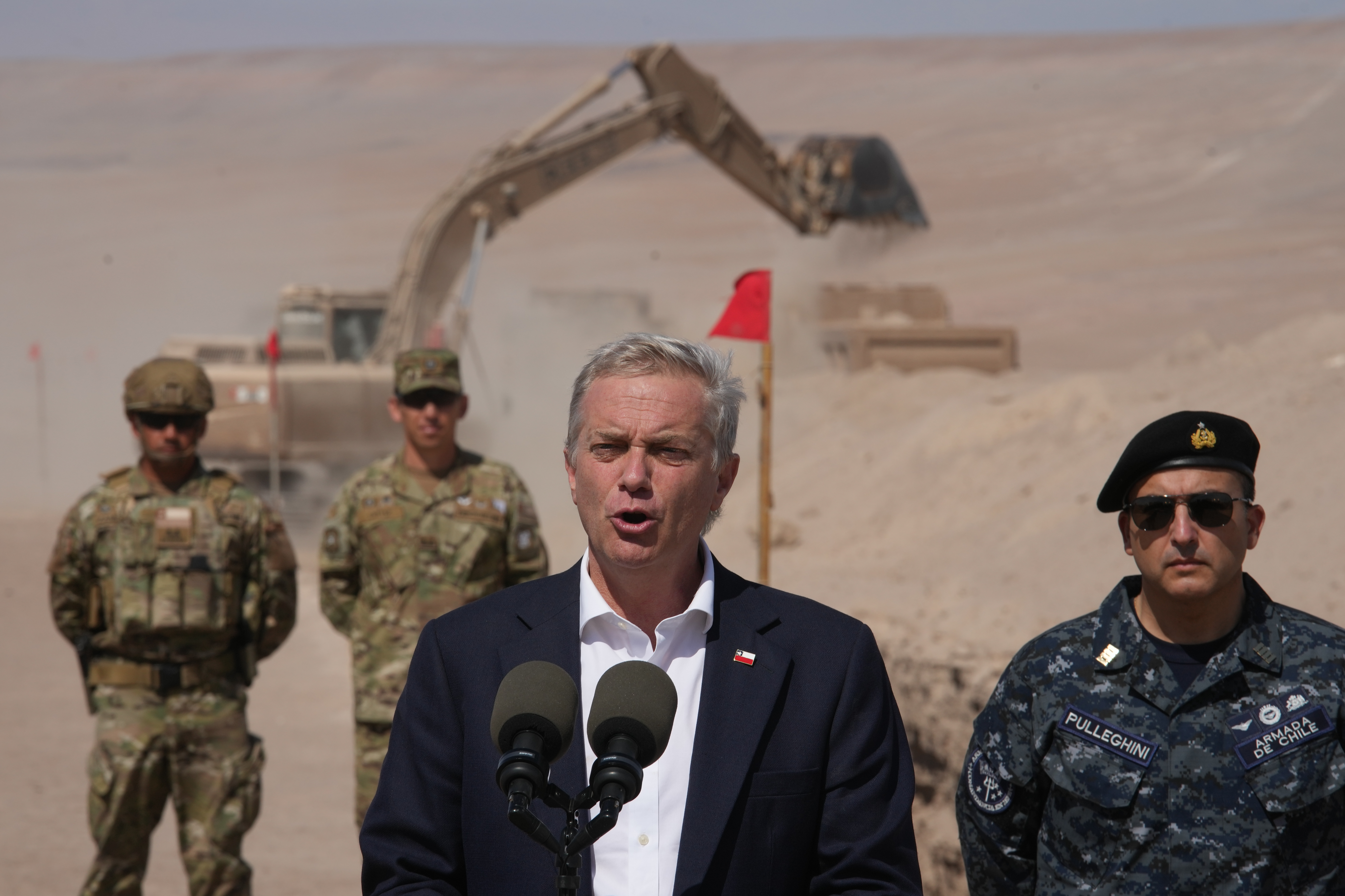 Chilean President Jose Antonio Kast gives a press conference while a machine digs, as part of measures to deter irregular migration along the northern border at the Chacalluta border crossing, in Arica, Chile, Monday, March 16, 2026. (AP Photo/Esteban Felix)