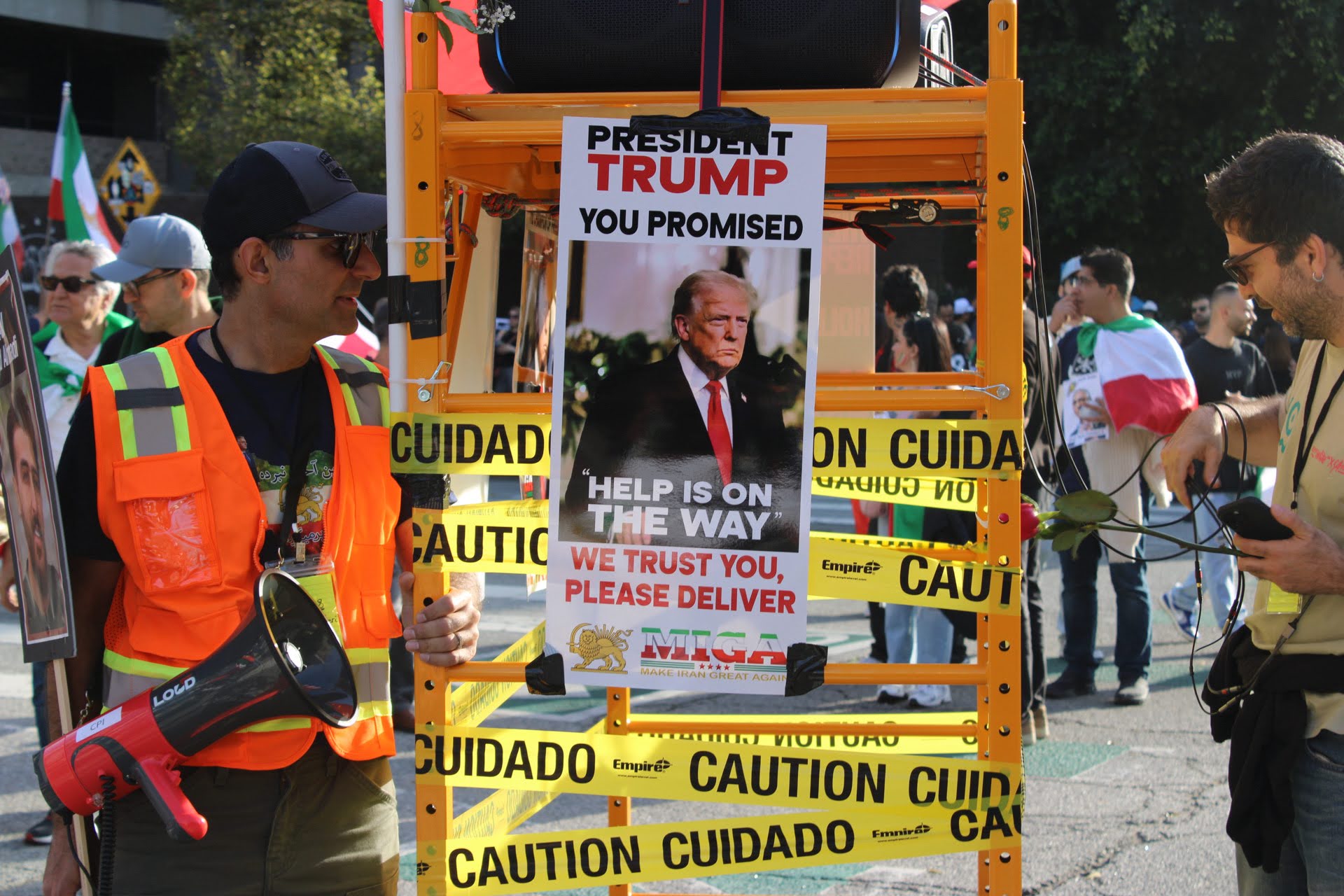 A protester in an orange reflective vest stands next to a sign featuring Trump's face and a pro-intervention message