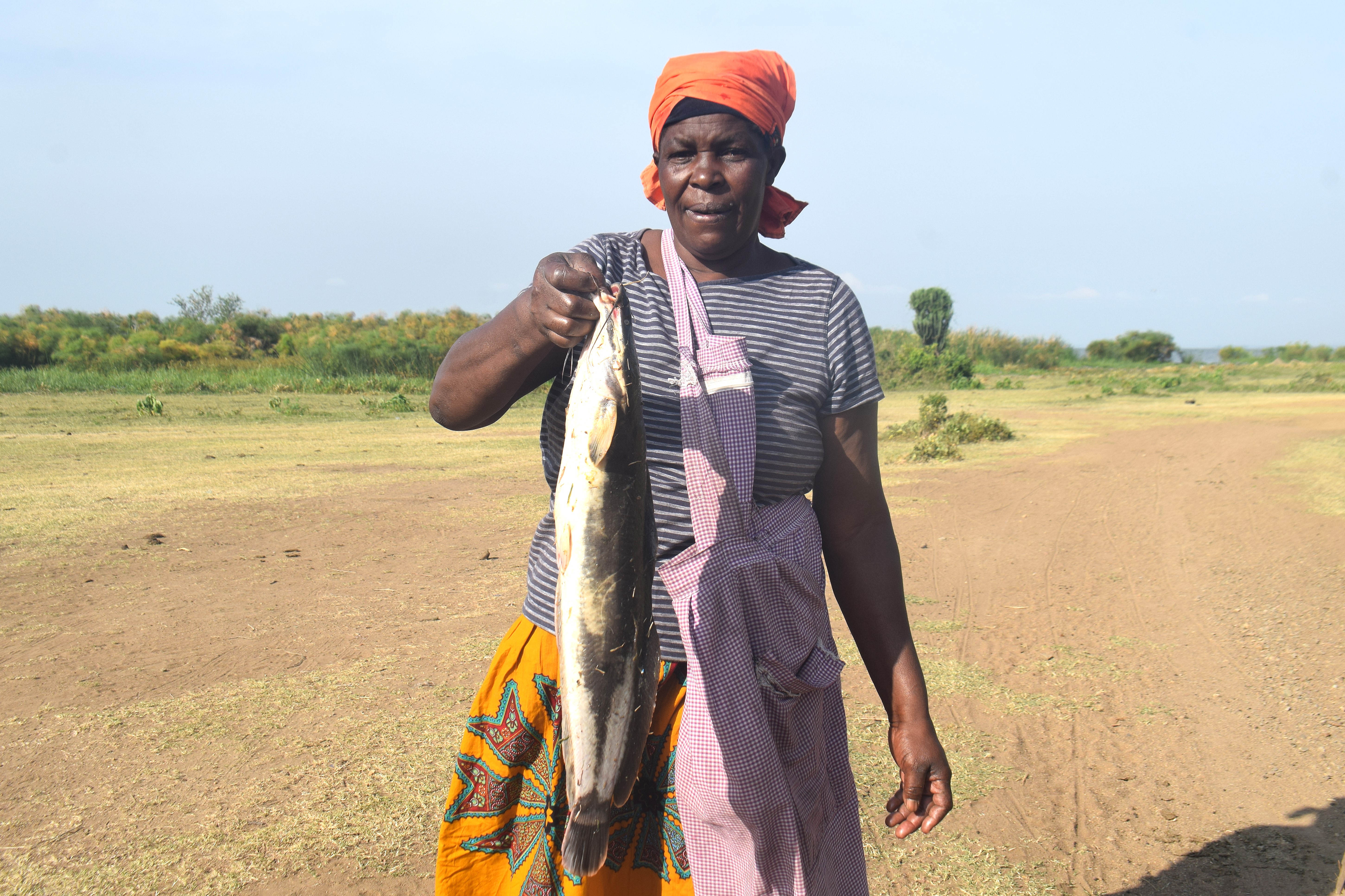 Rhoda Ongoche Akech, 61, holds one of the fish varieties found in Lake Victoria at Kagwel Beach, Kisumu, Kenya