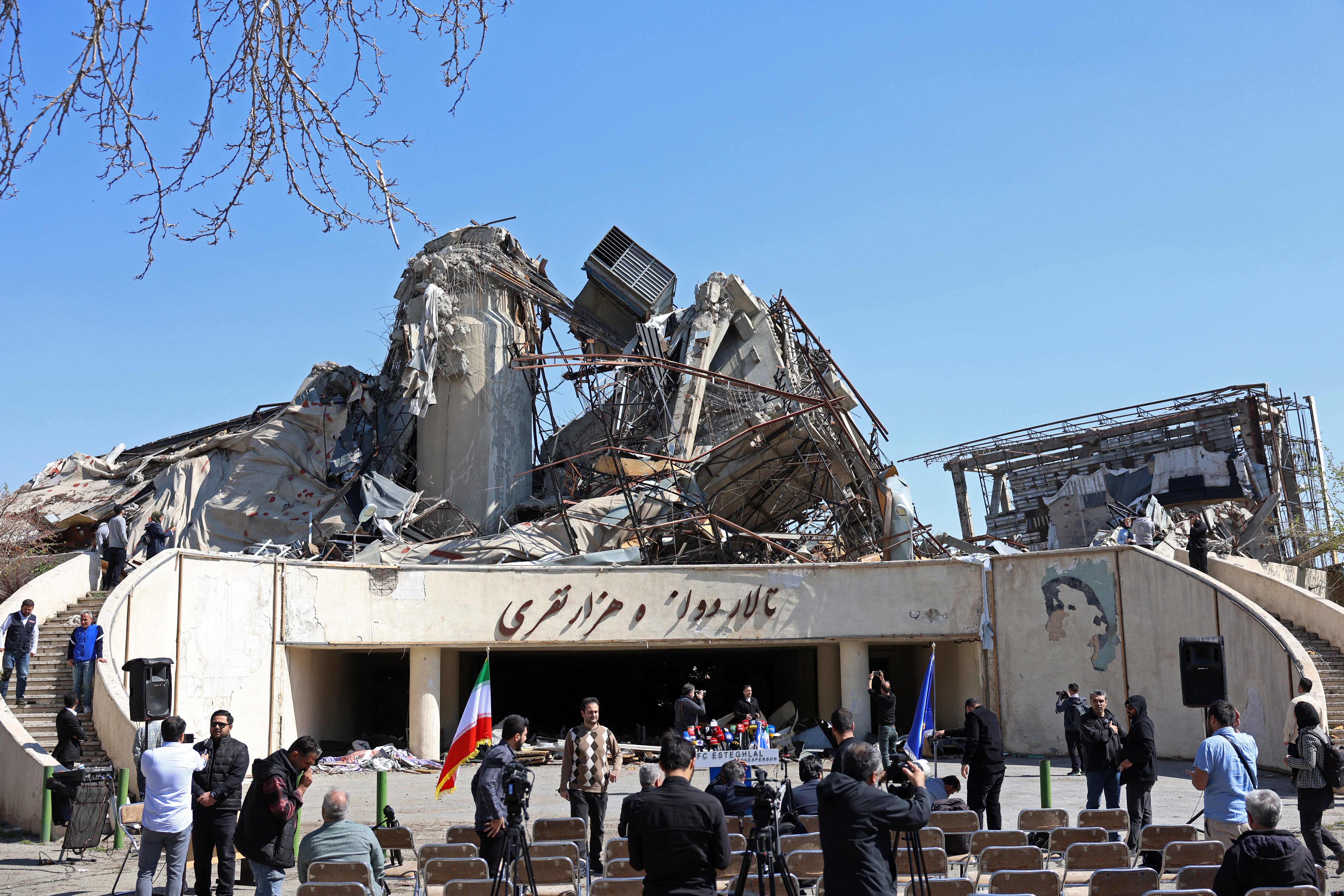 Media representatives gather in front of a heavily damaged building following a strike at the Azadi Sport Complex in Tehran on April 3, 2026.