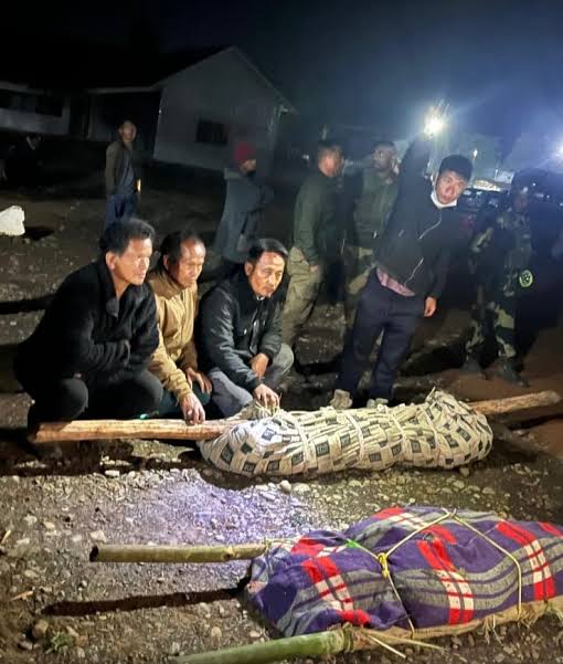 Men sit beside the bodies of two labourers killed in Ukhrul in March 2026