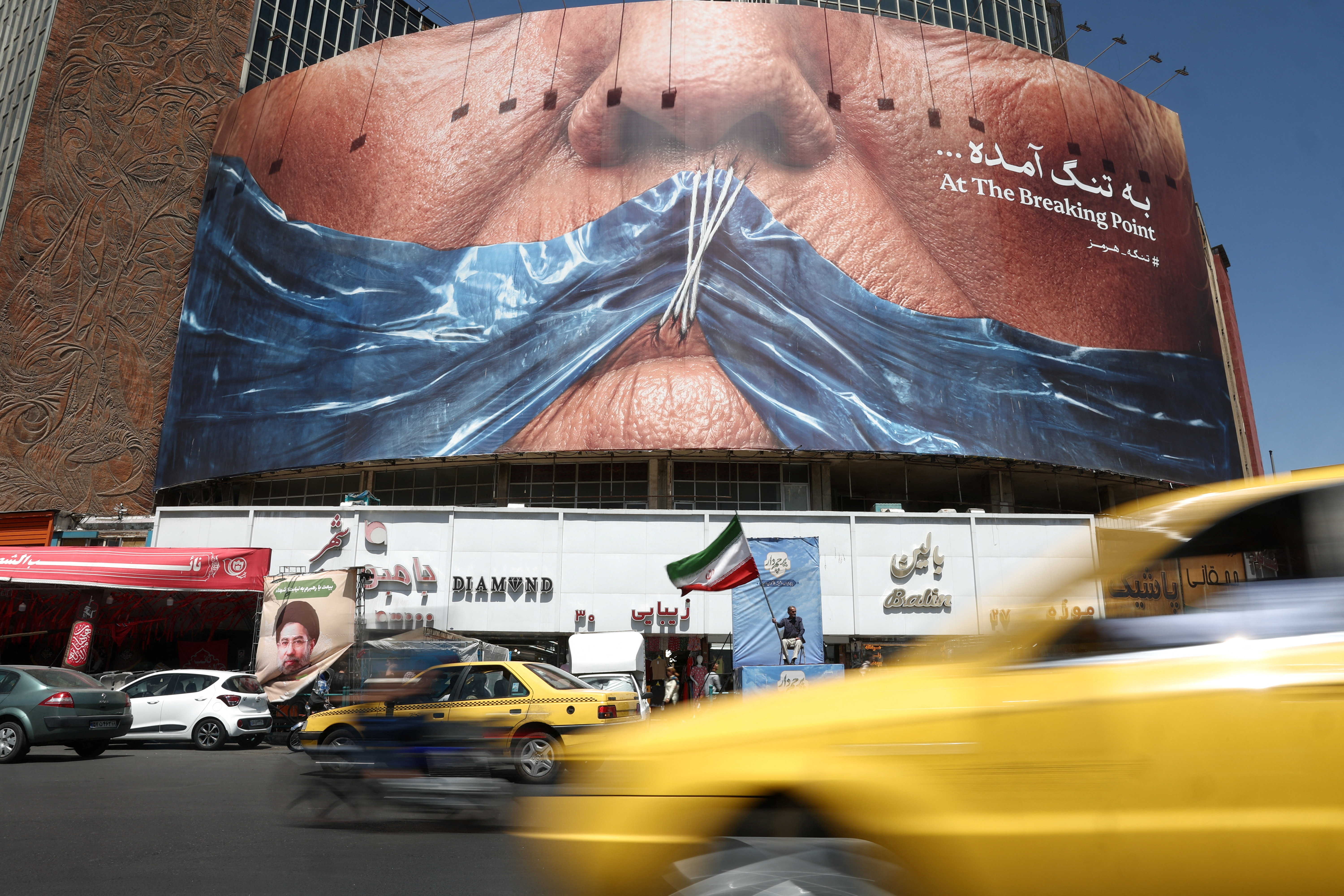 People ride past an anti-U.S. billboard depicting U.S. President Donald Trump and the Strait of Hormuz