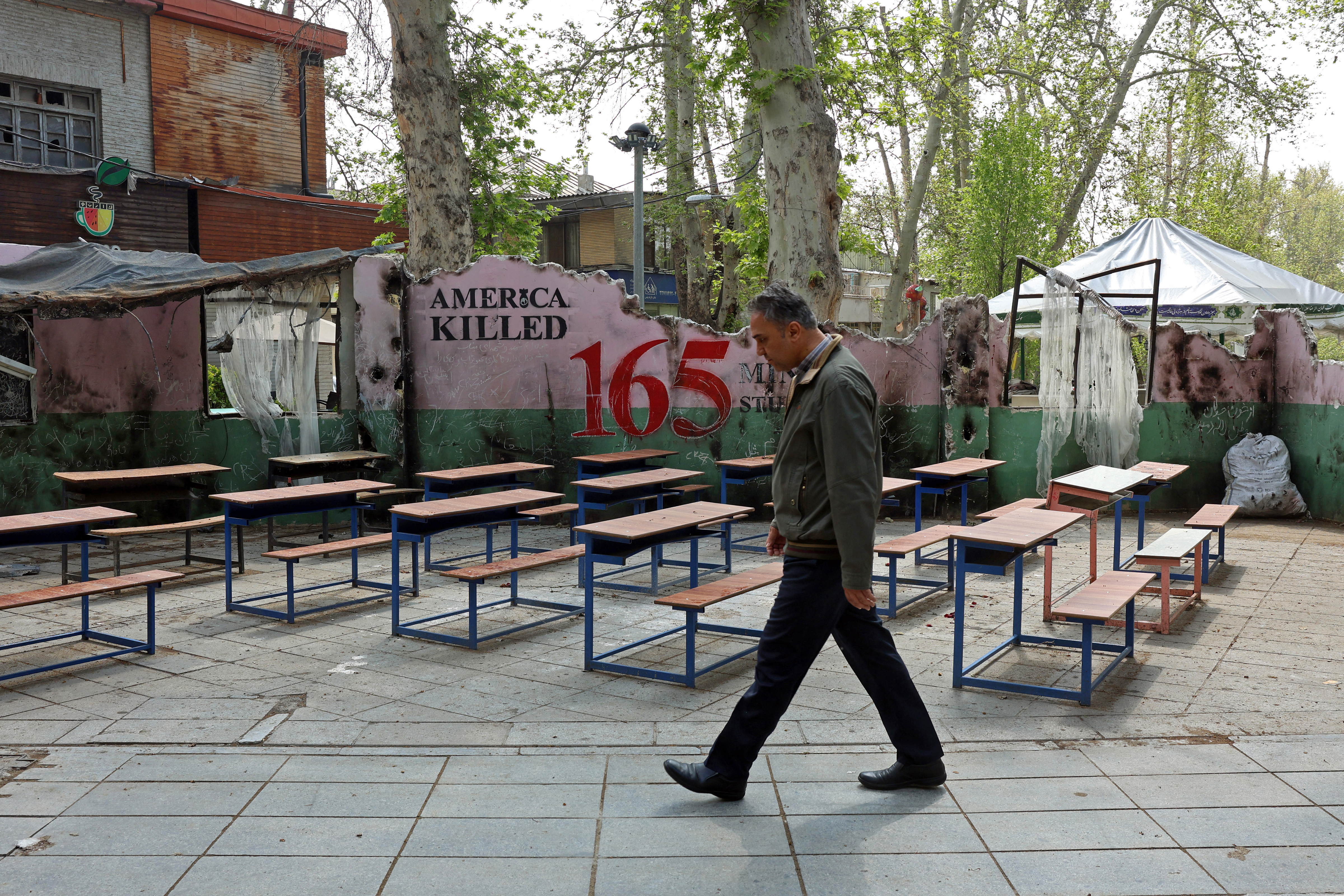 A man walks past a memorial depicting a symbolic classroom representing the Minab school children is displayed in a square in Tehran on May 3, 2026. Iran on April 28 shared a breakdown of the death toll from the deadly strike on the school on the first day of the Middle East war. Seventy-three boys and 47 girls were killed in the February 28 strike in Minab, state broadcaster IRIB and local media reported. The attack happened on the day the United States and Israel launched attacks across Iran. In retaliation, Tehran struck targets in Israel and Gulf nations. (Photo by AFP) /