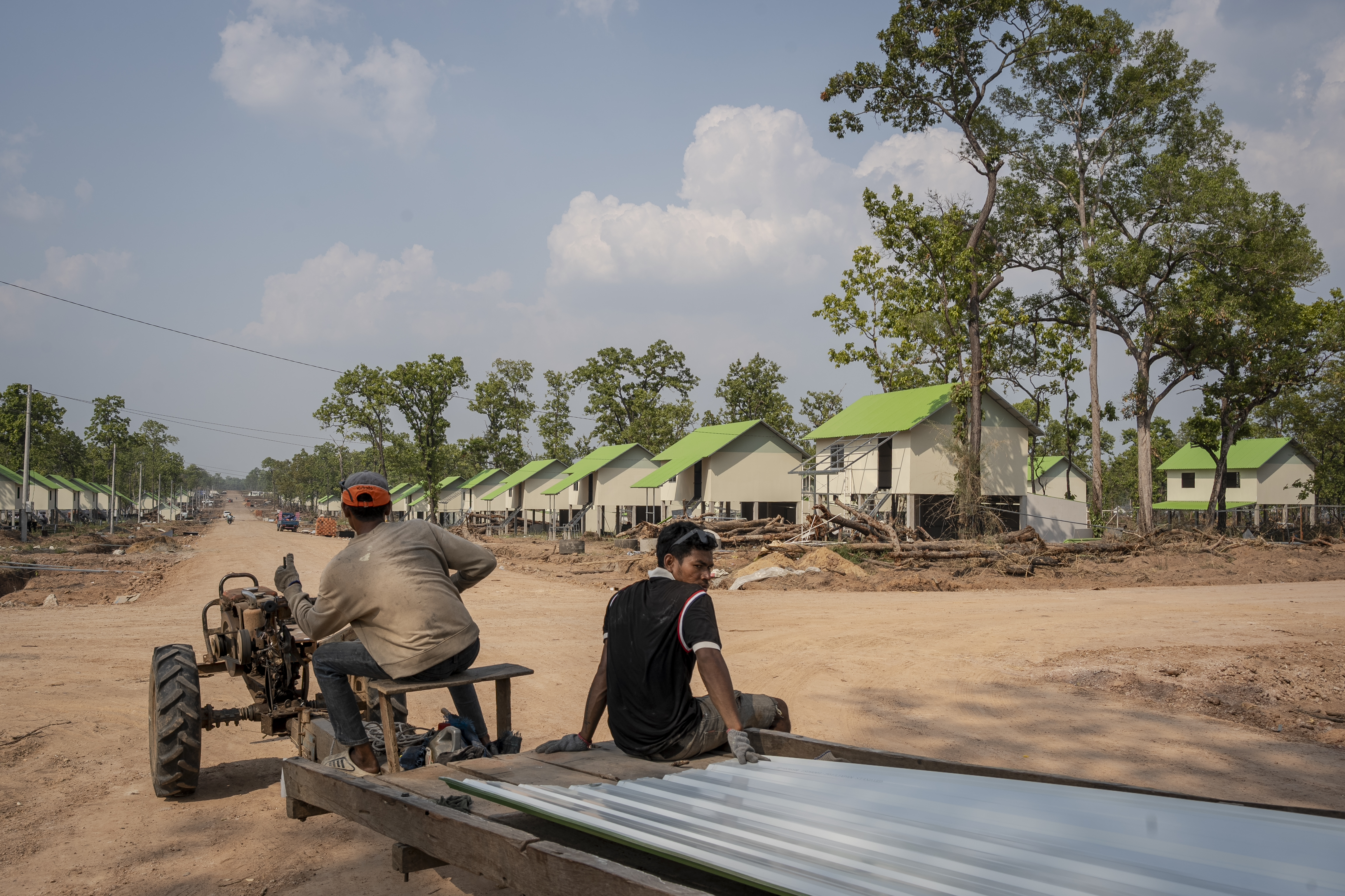 Two construction workers transport corrugated metal sheeting between the newly constructed resettlement houses for displaced Cambodians in Preah Vihear province