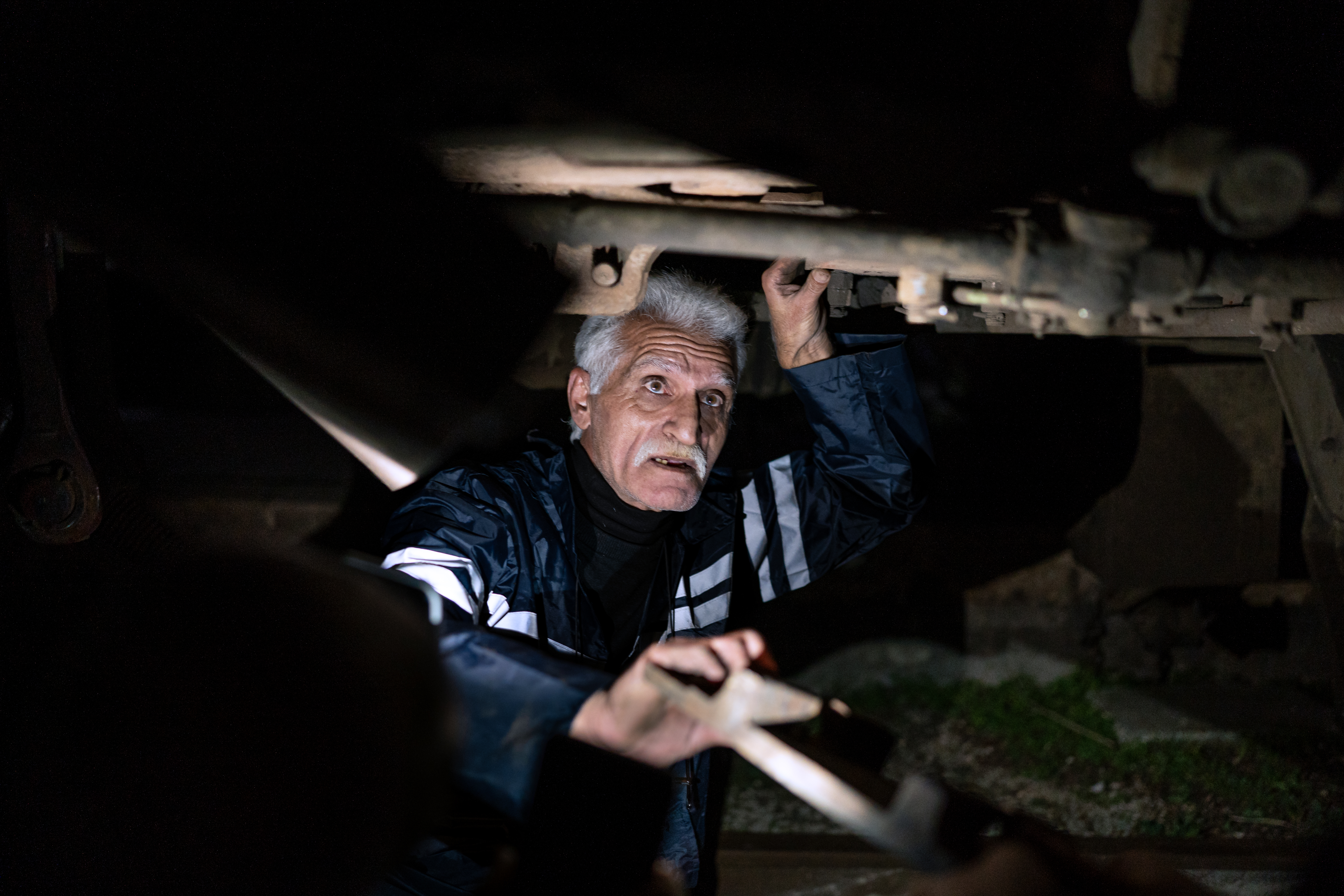 Relief train driver Motaz Hassan makes repairs under the locomotive after the crash [Charles Cuau/Al Jazeera]