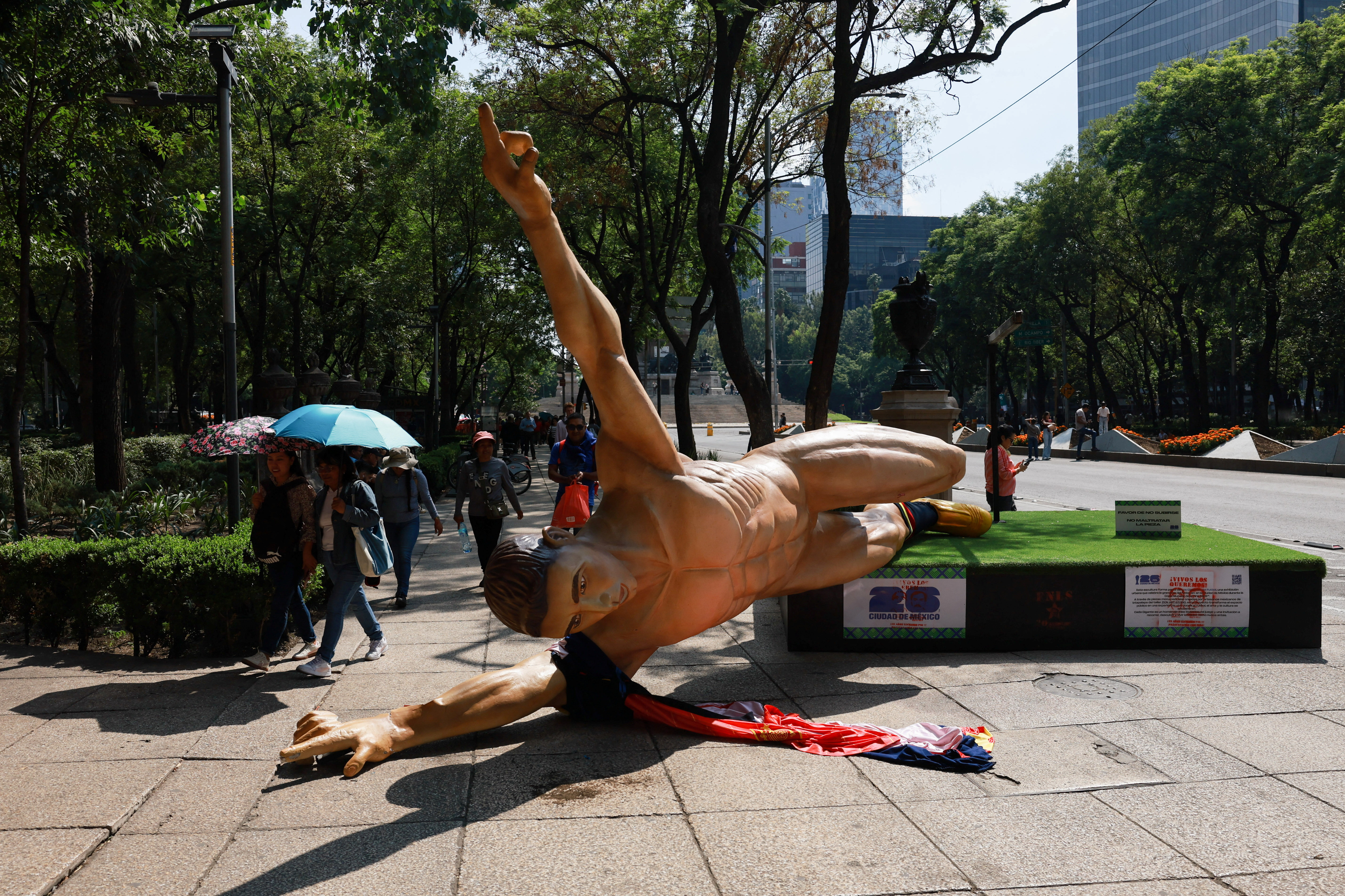 People walk near the fallen statue of a soccer player