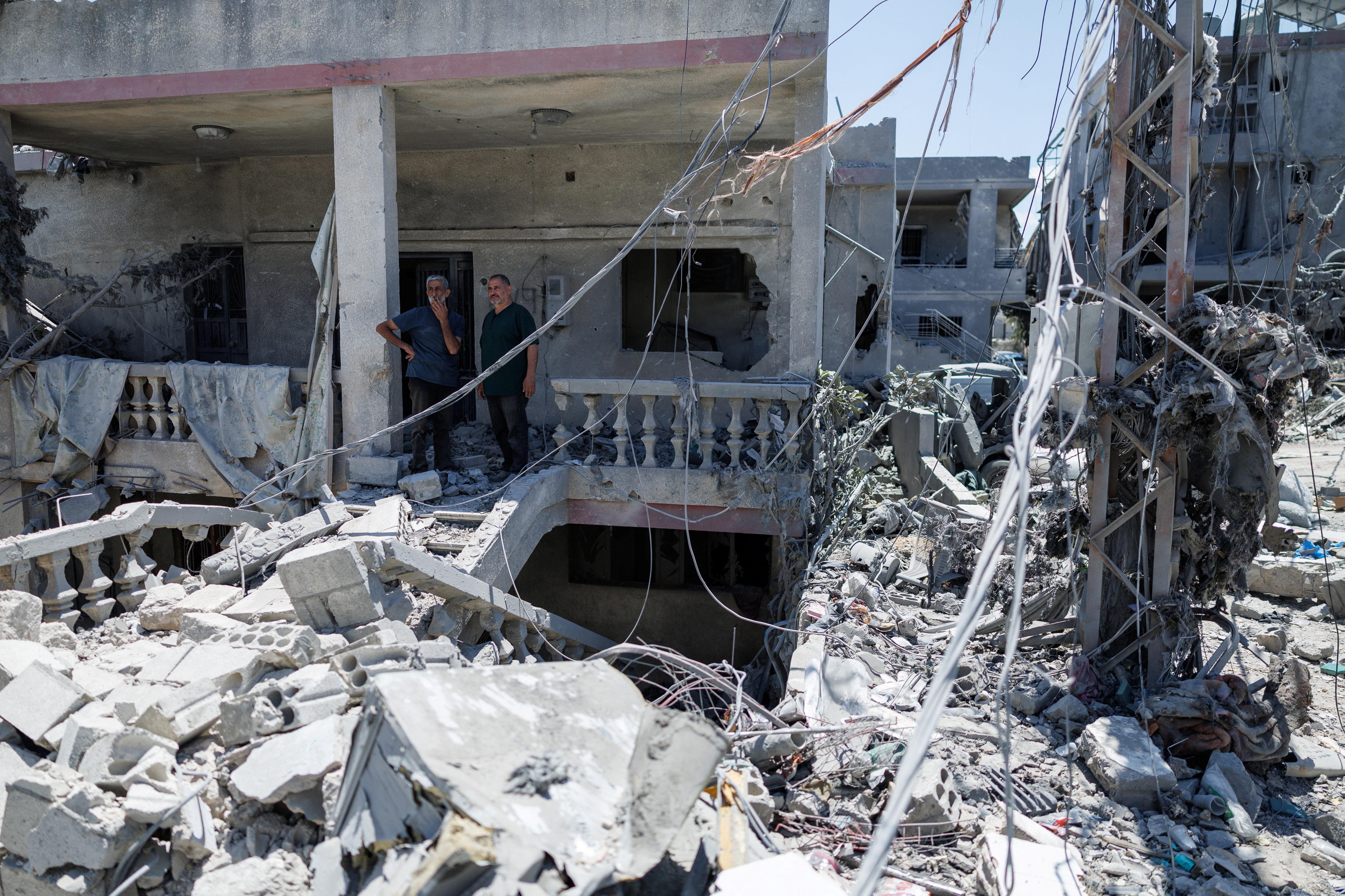 A man smokes a cigarette as he stands with a relative at his house, damaged by an Israeli air strike, while they look at neighbouring houses that were destroyed. The men returned to their village after being displaced by the war, following the deal between the US and Iran, in Qlailieh, Tyre district, Lebanon, June 18, 2026