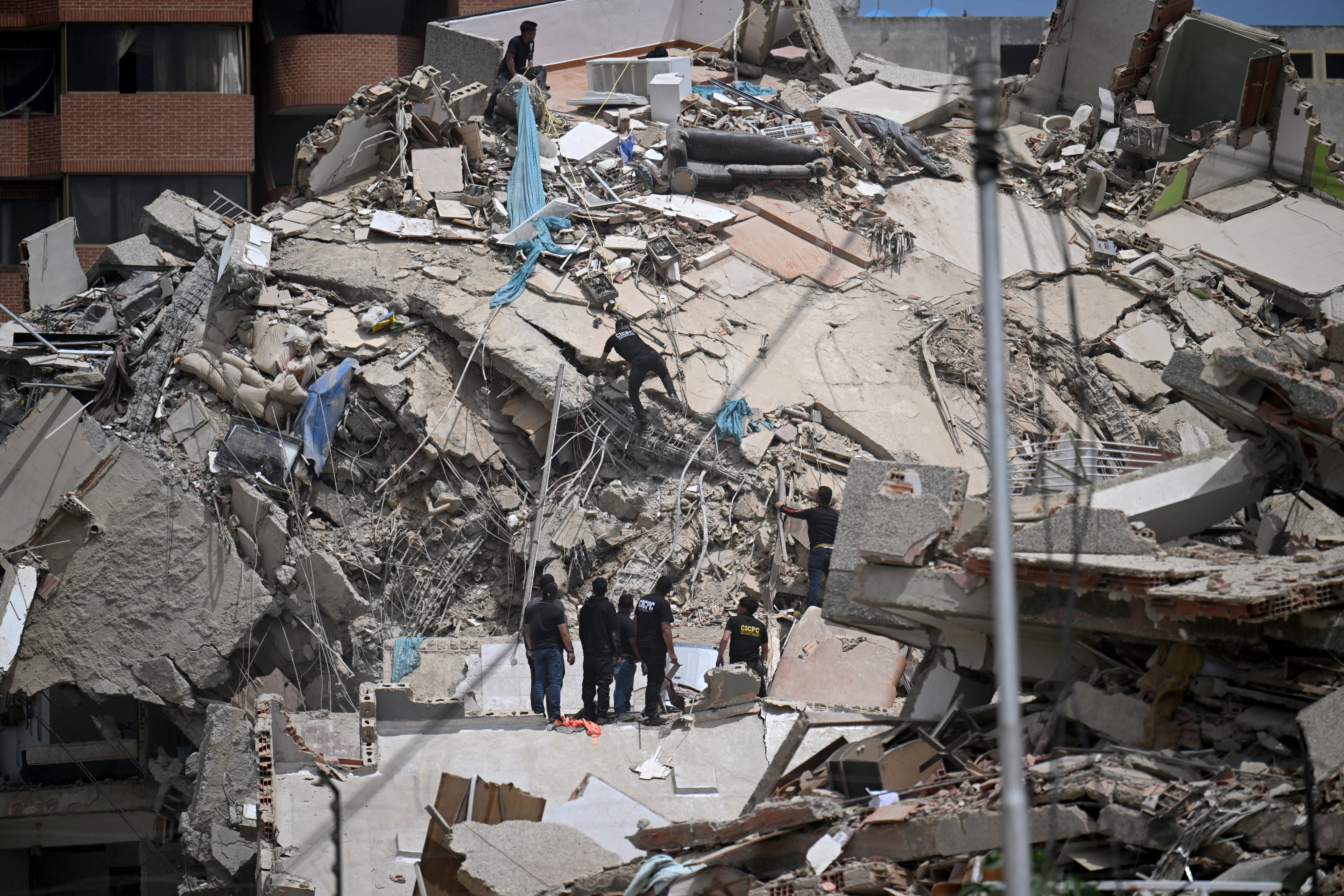 Rescue workers search across the slab of a collapsed building amid twisted rebar and debris following an earthquake in Catia La Mar, La Guaira state, about 30 km northwest of Caracas, on June 25, 2026.