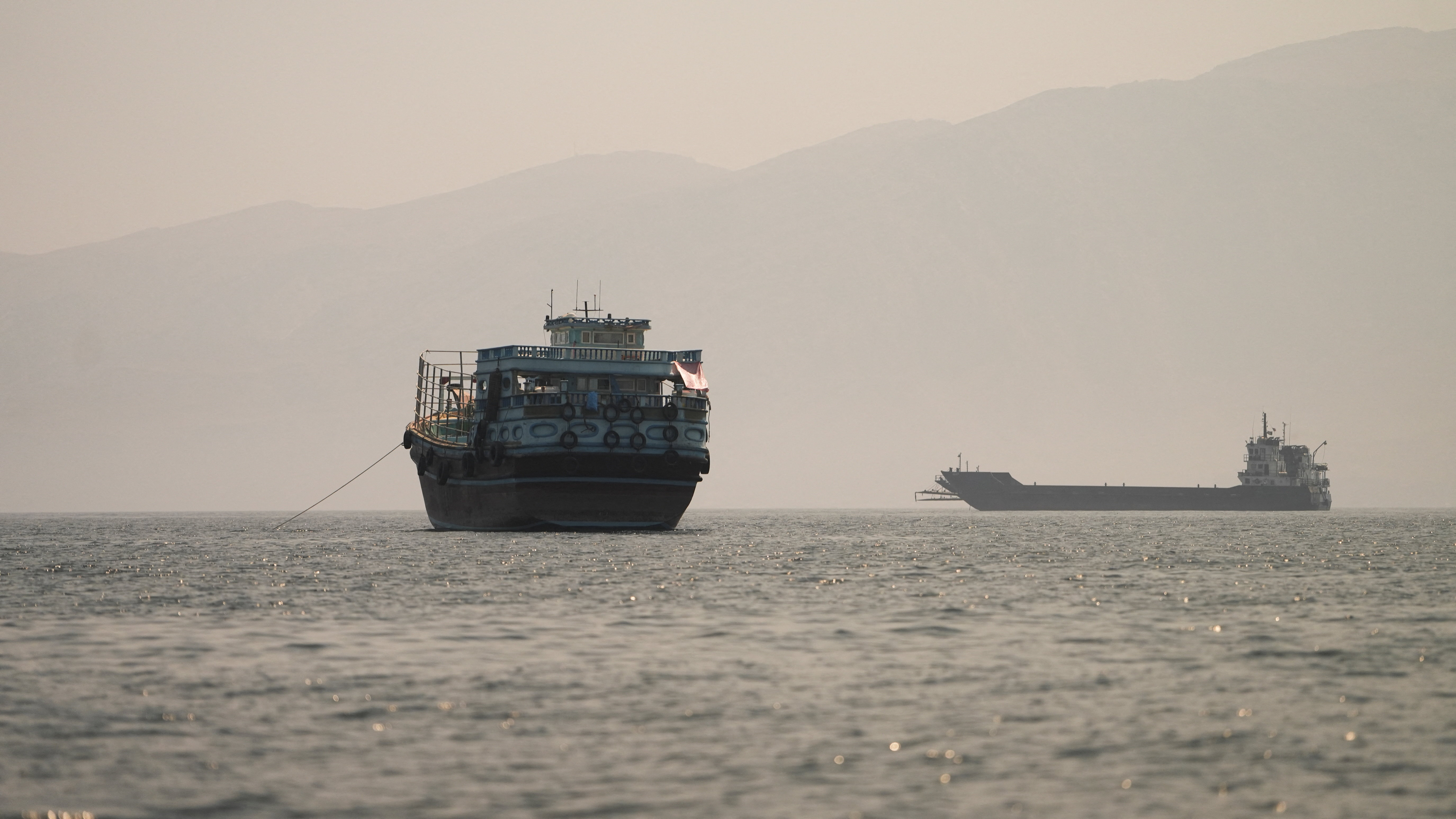 Cargo vessels move through the waters of the Strait of Hormuz, viewed from a rocky coastline.