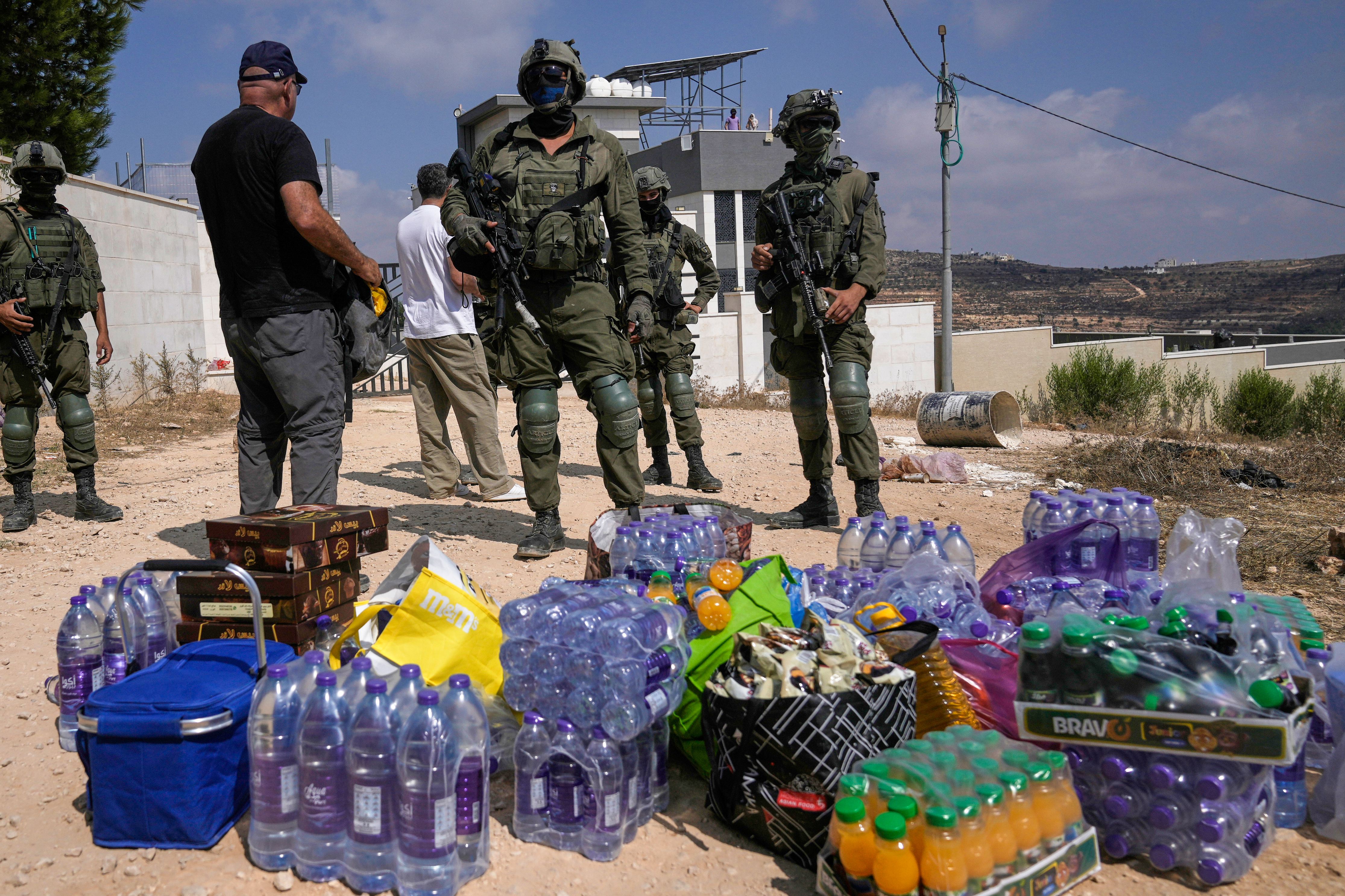 Activists accumulate food and water supplies in front of Israeli army soldiers who are blocking the road leading to the houses of three Palestinian families that have been besieged by Israeli settlers for six days, in the occupied West Bank village of Qusra, south of Nablus, Friday, Aug. 14, 2026. (AP Photo/Majdi Mohammed)