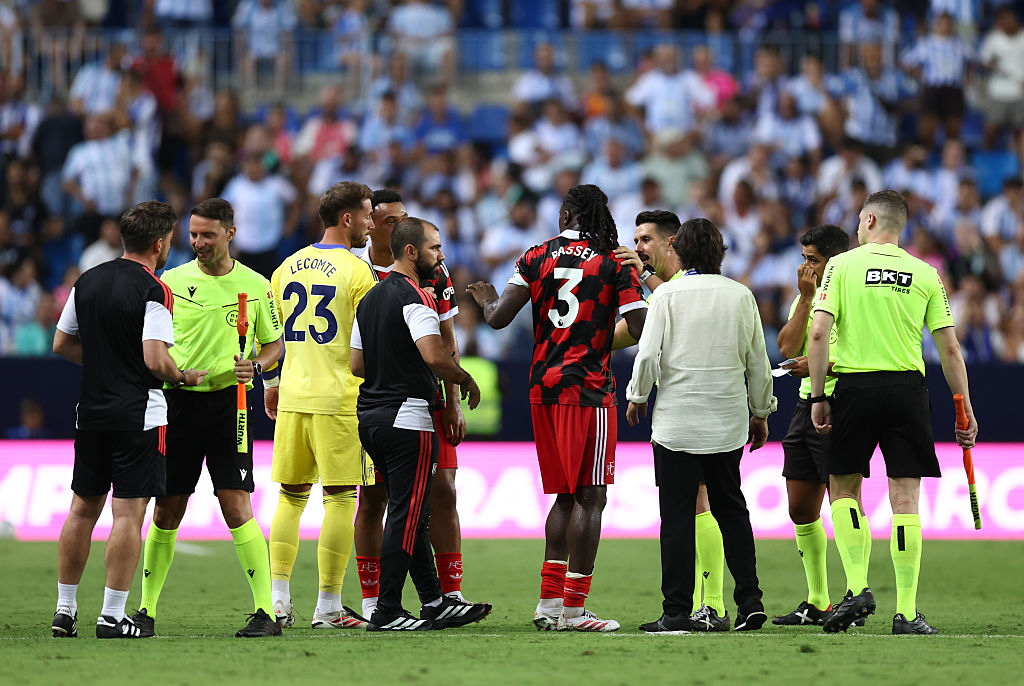 A group of players and officials stand on a football pitch