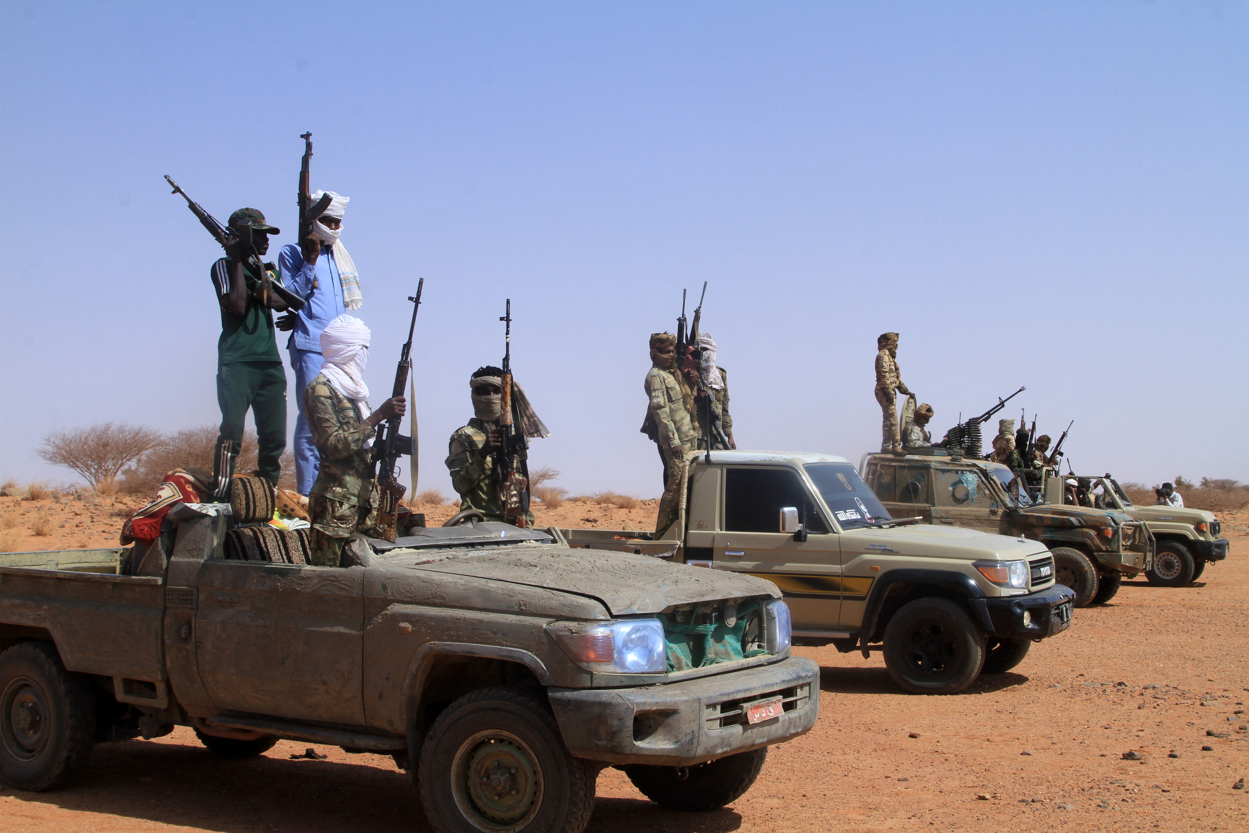 A group of armed men stand on vehicles.