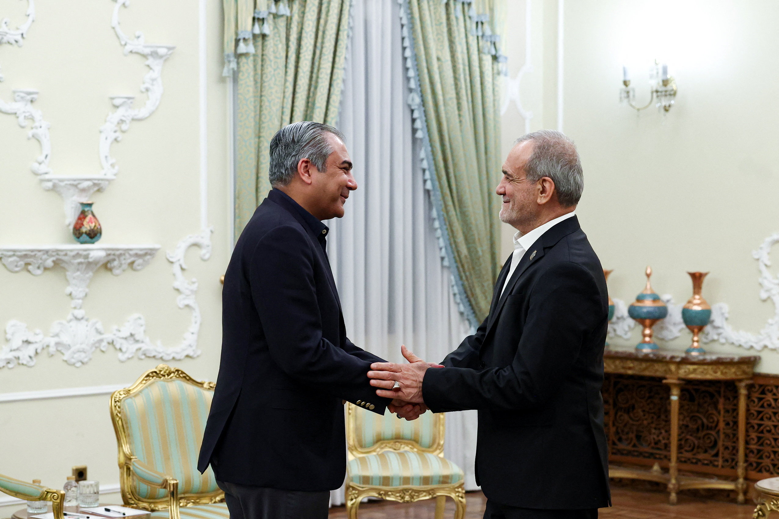 Iranian President Masoud Pezeshkian shakes hands with Pakistan's Interior Minister Mohsin Naqvi.