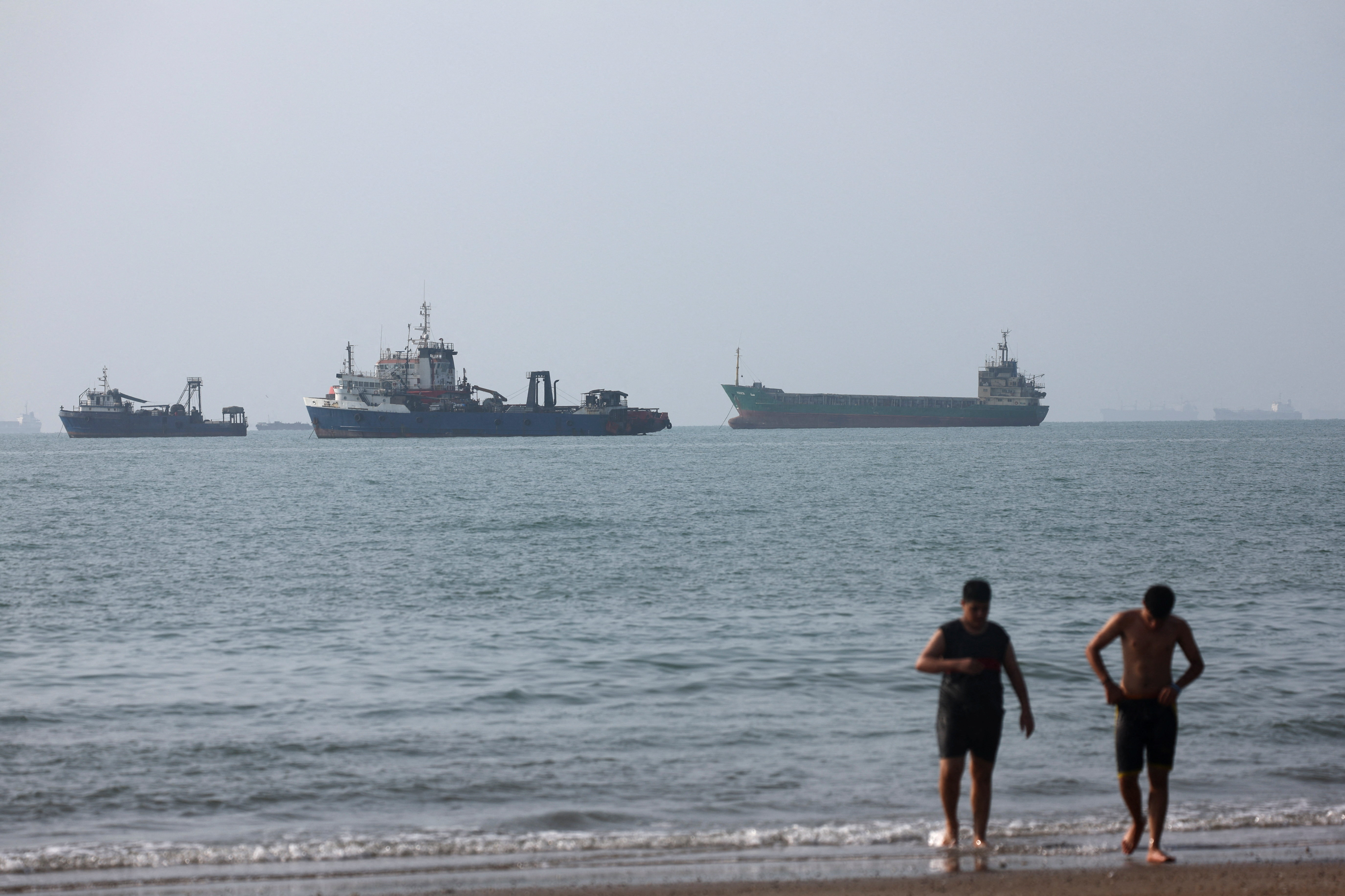 Two men come out of the sea with ships visible behind them.