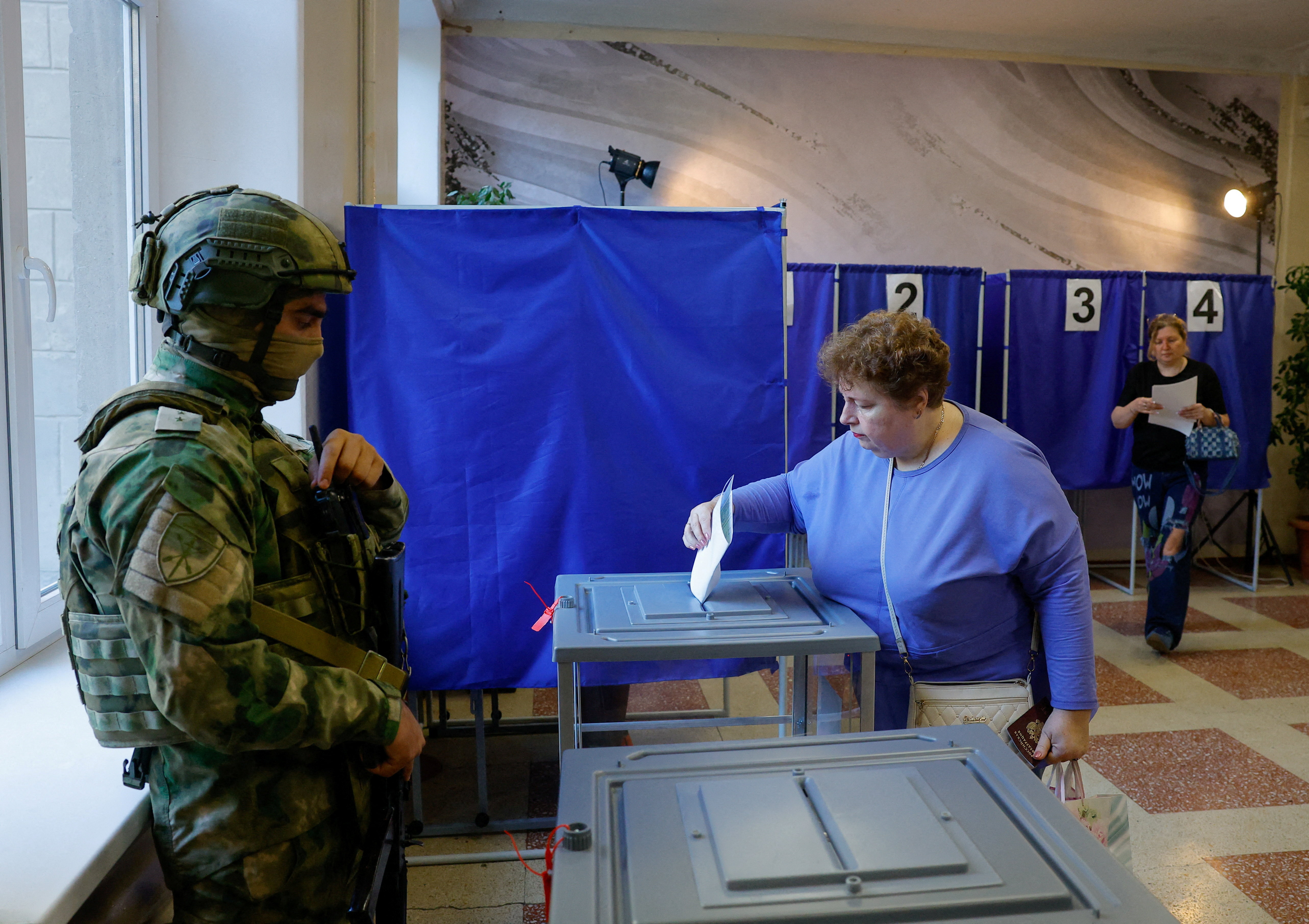 A woman casts her ballot next to a serviceman securing a poling station during Russia's parliamentary elections, in the course of Russia-Ukraine conflict in Donetsk, Russian-controlled Ukraine, September 18, 2026. REUTERS/Alexander Ermochenko TPX IMAGES OF THE DAY