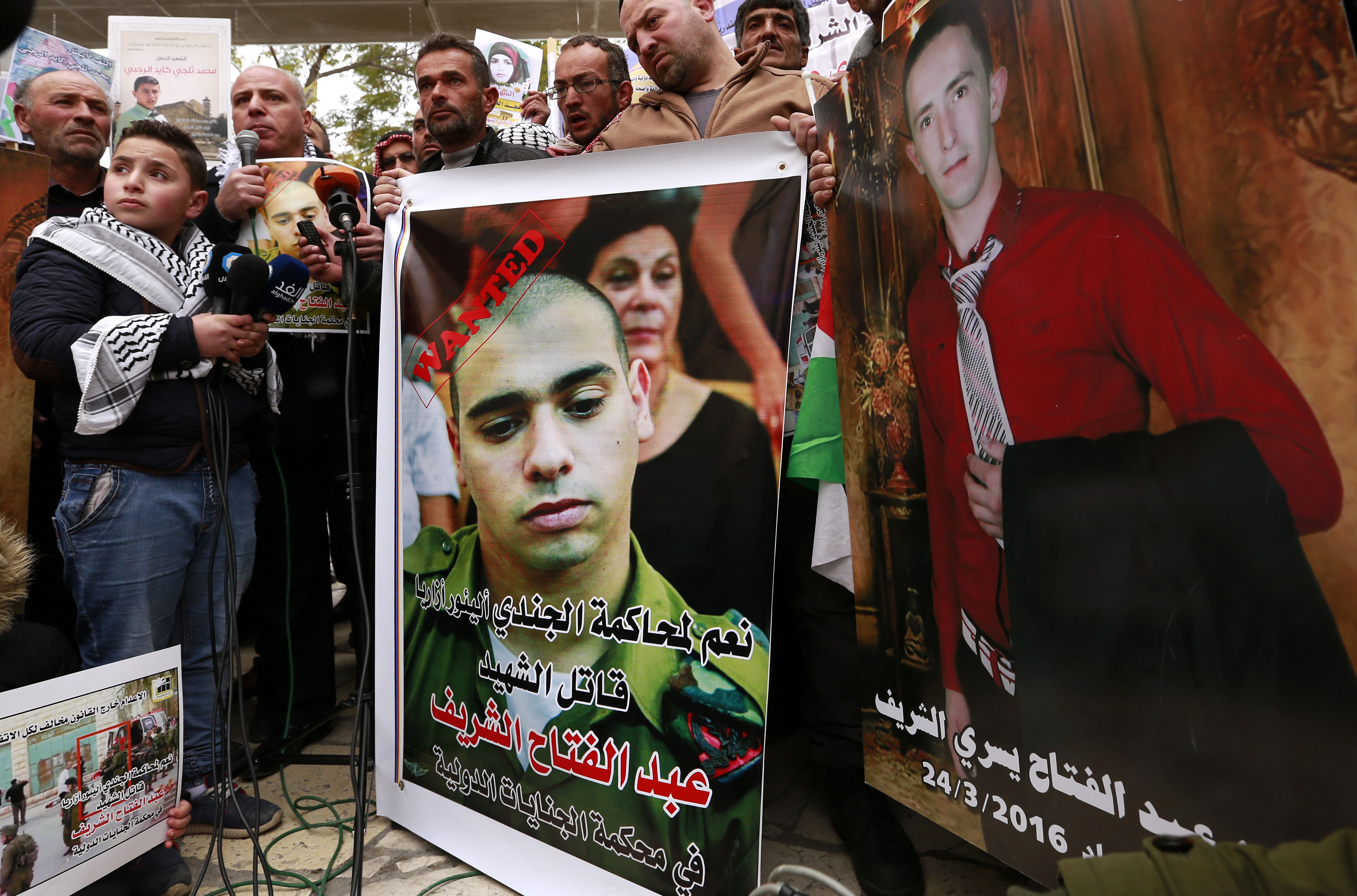 Palestinians hold placards against Israeli Sergeant Elor Azaria, who shot and killed an injured Palestinian man (in picture on right), during a protest in the West Bank city of Hebron [Abed al Hashlamoun/EPA]