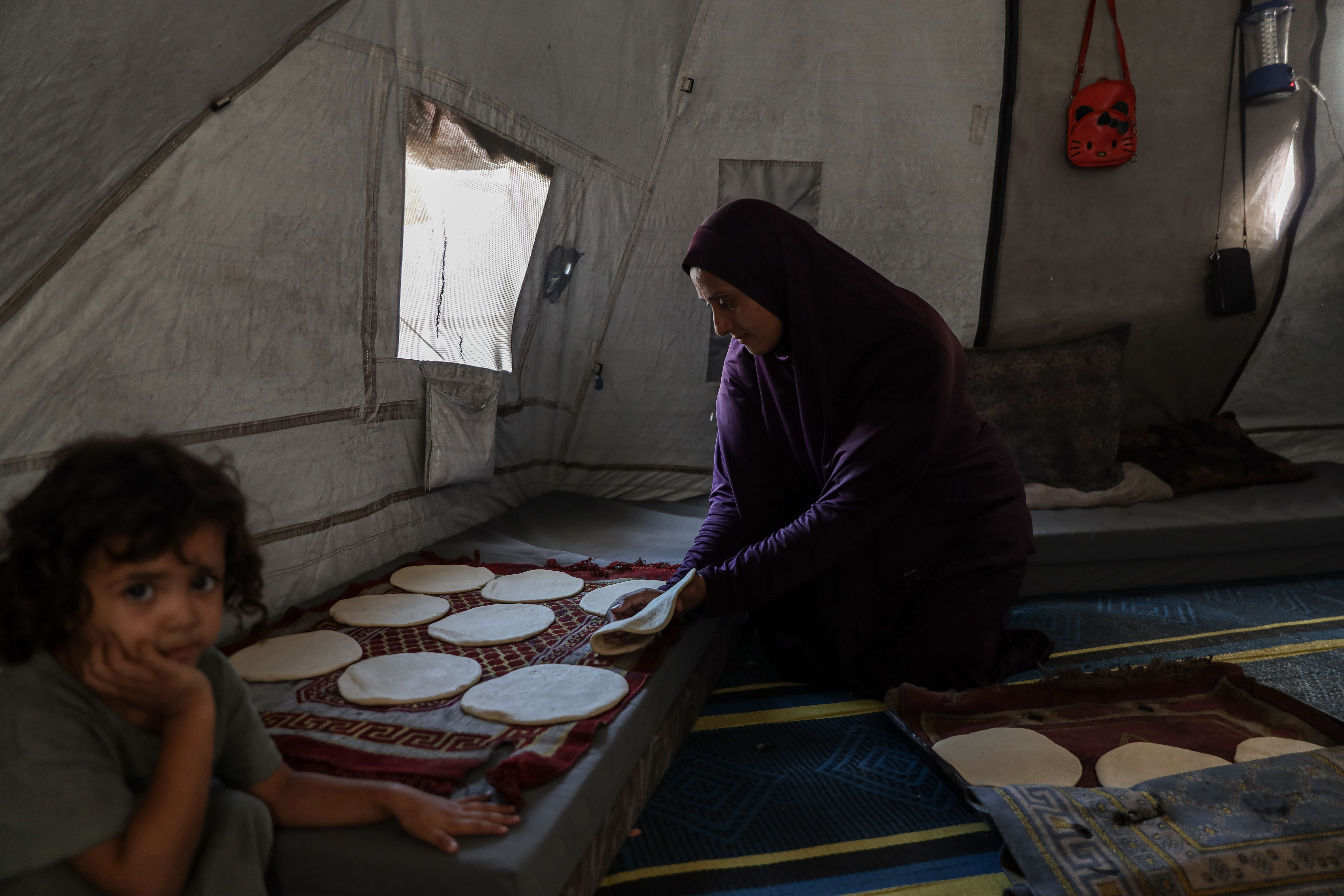 Azza Ashour, 31, kneads dough inside her tent at a school shelter in Gaza, preparing bread for her five children