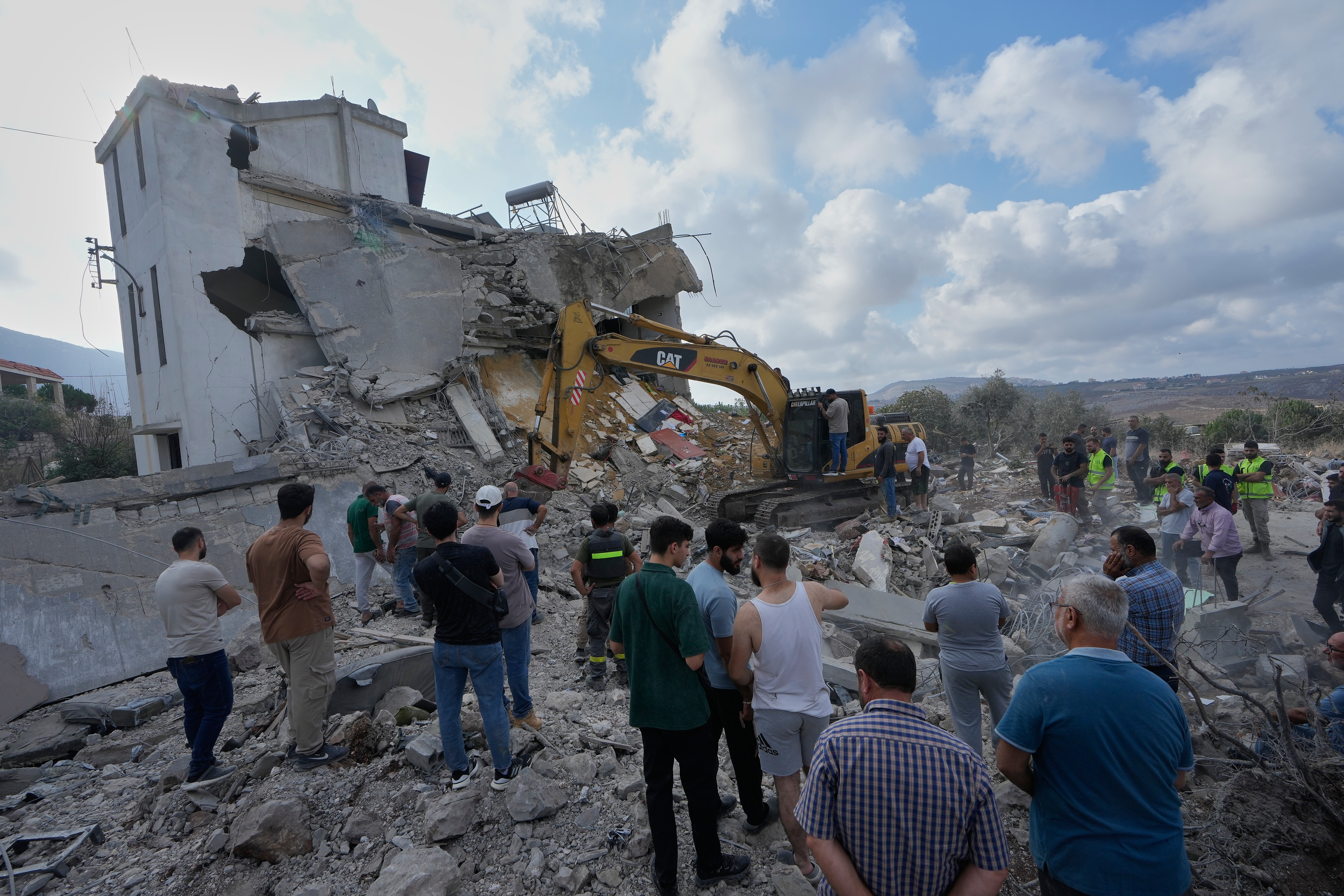 People watch rescue workers use an excavator as they conduct a search operation at a destroyed house