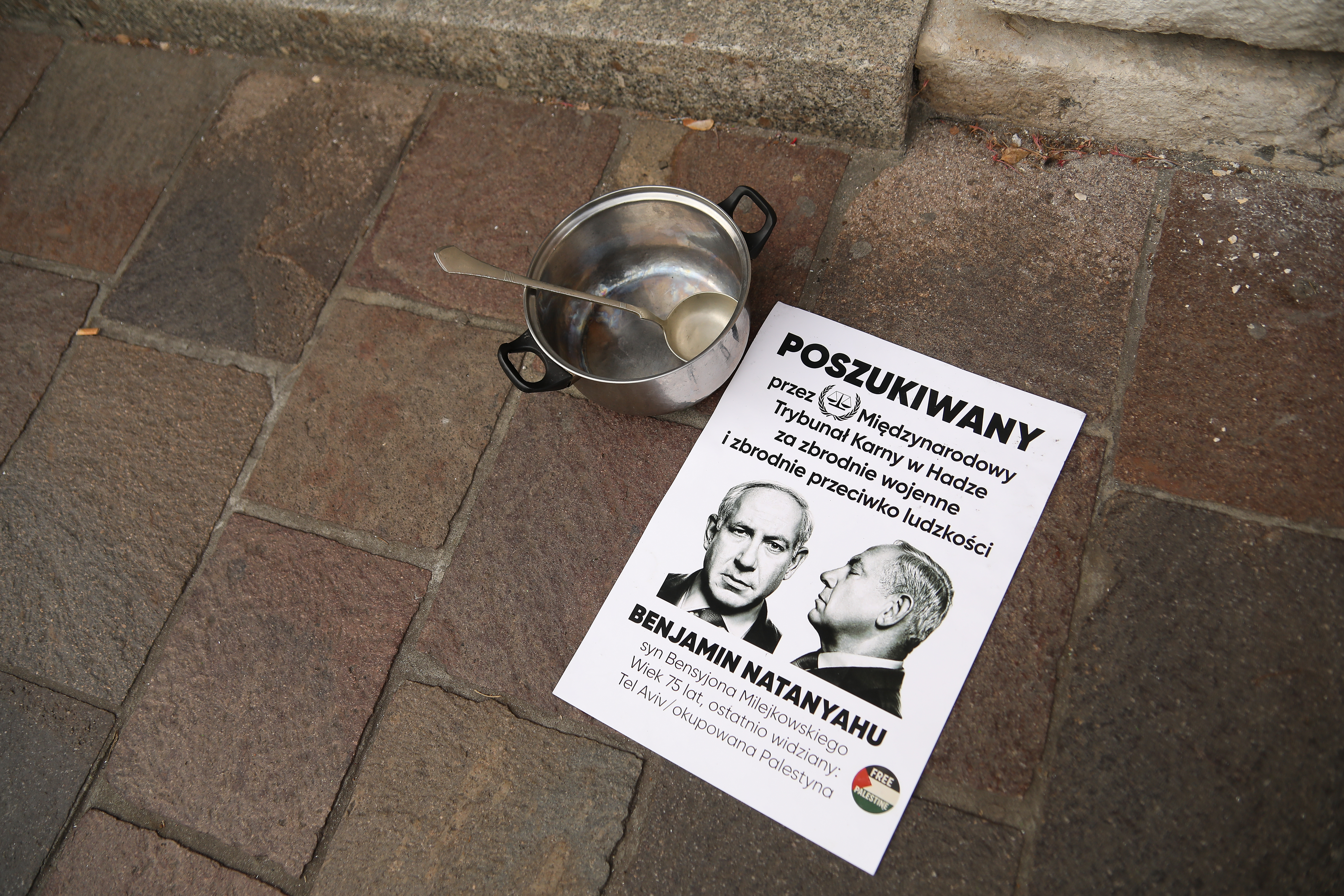 A poster announces that Benjamin Netanyahu is wanted by the International Criminal Court, and a pot with a spoon is seen during a pro-Palestinian protest disrupting the US Consulate with noise on October 6, 2025, in Krakow, Poland. A pro-Palestinian protest takes place in front of the US Consulate in Krakow. Participants disrupt the facility with the noise of clanging pots and loudspeakers. Protesters speak about US support for Israel and, in their view, US complicity in the genocide in Gaza. The International Association of Genocide Scholars (IAGS) and the UN Commission declare that Israel's actions in the Gaza Strip meet the legal definition of genocide. The prosecutor of the International Criminal Court requests the issuance of an arrest warrant for Israeli Prime Minister Benjamin Netanyahu. (Photo by Klaudia Radecka/NurPhoto via Getty Images)