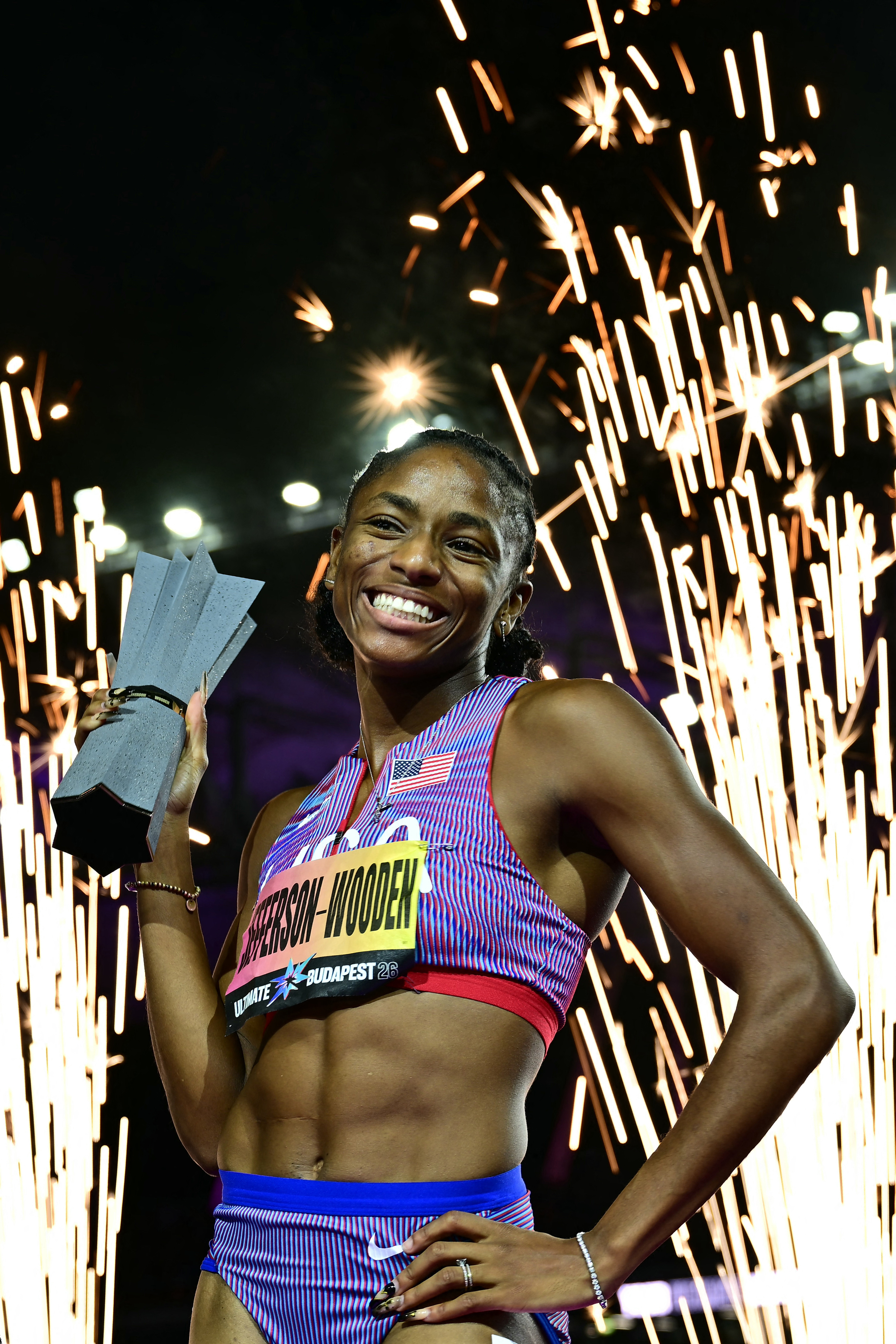 Melissa Jefferson-Wooden smiles and holds up a trophy on the track