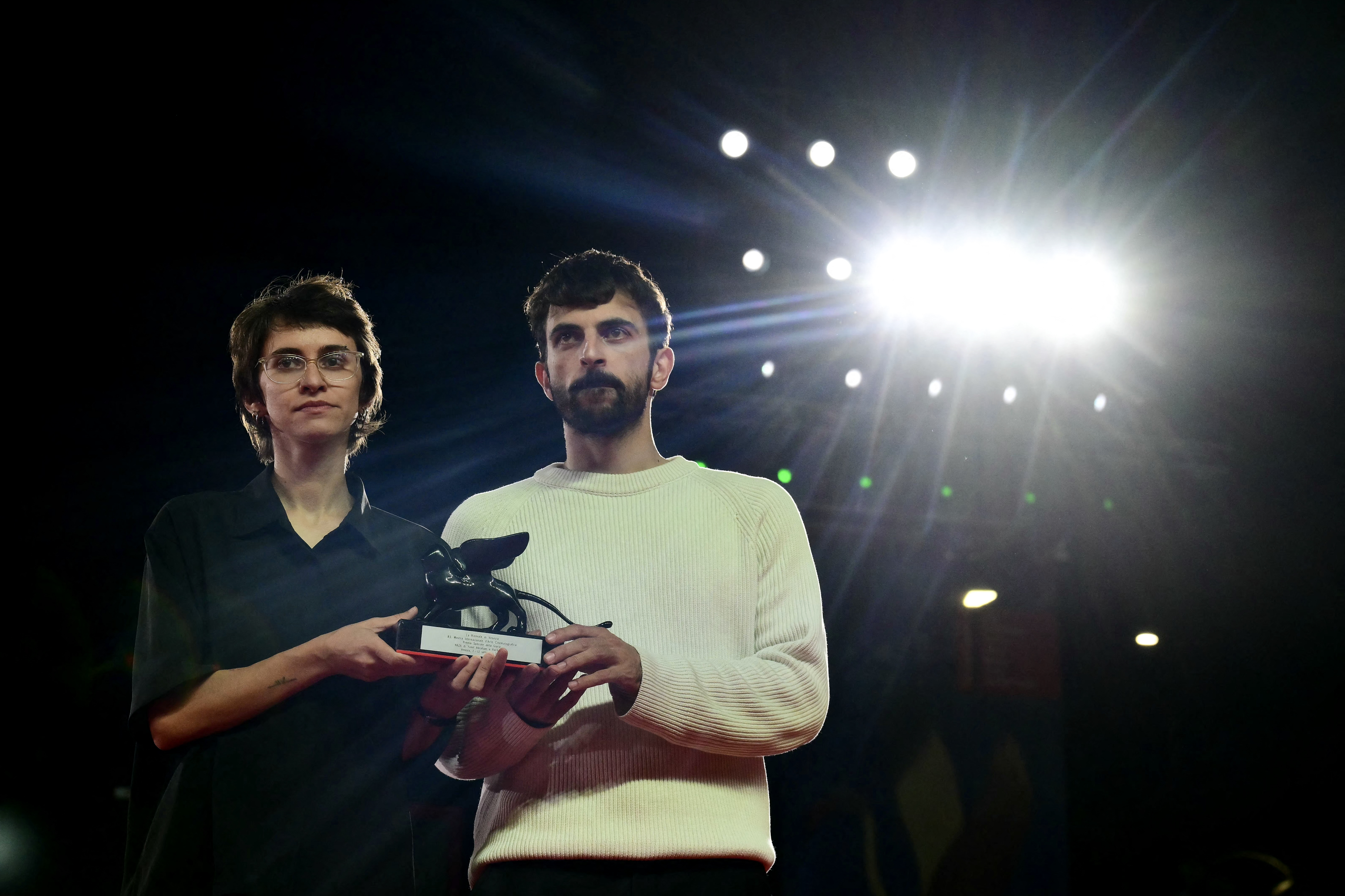 Two people stand side by side holding an award at a film festival photocall.
