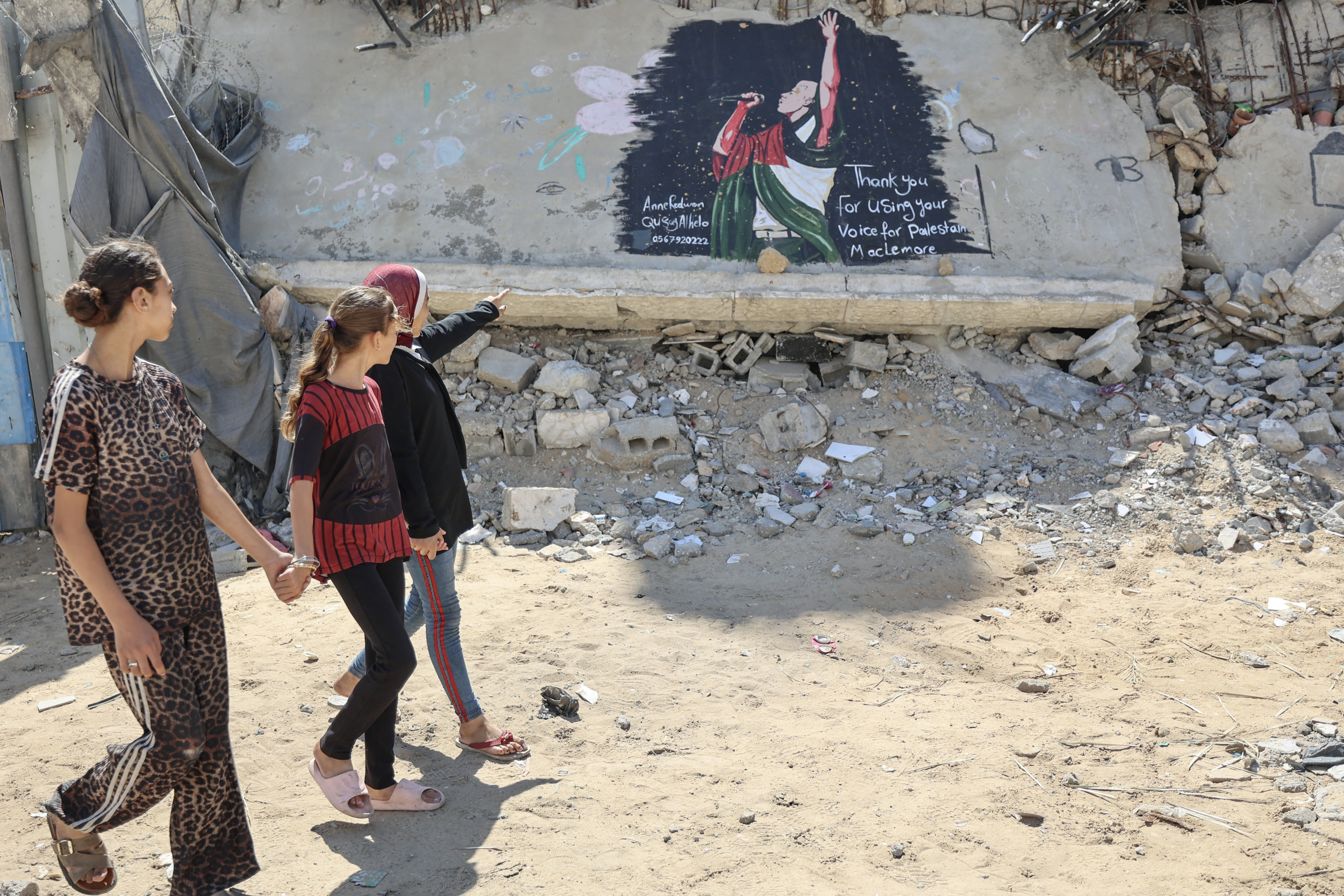 Palestinian girls walk past a mural painted on the rubble of a destroyed building and dedicated to US rapper, singer, dancer and DJ, Benjamin Haggerty, known as Macklemore, in Gaza City on September 19, 2026.