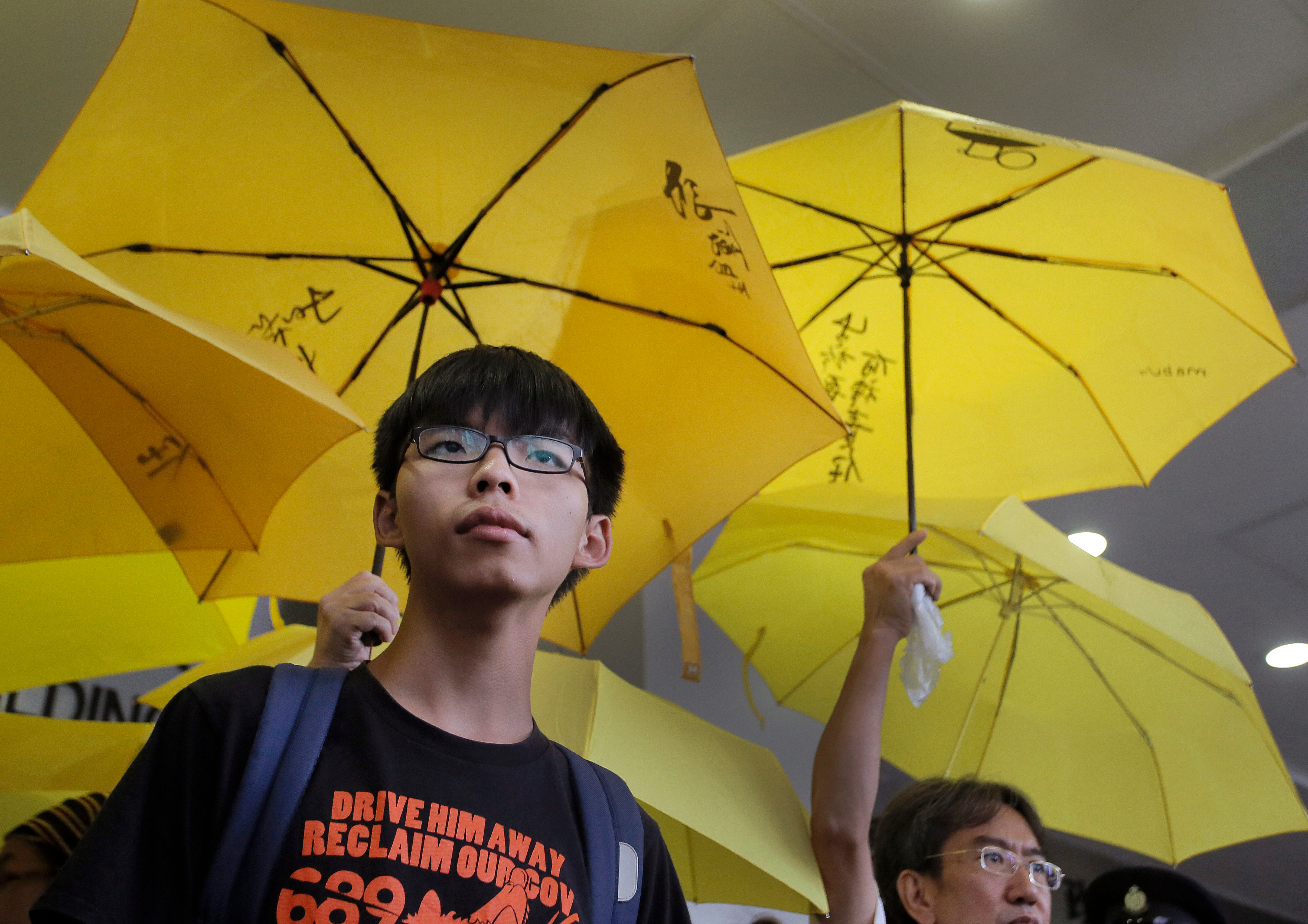 Hong Kong student leader Joshua Wong, left, stands in front of yellow umbrellas outside a magistrates' court in Hong Kong [File: Vincent Yu/AP Photo]