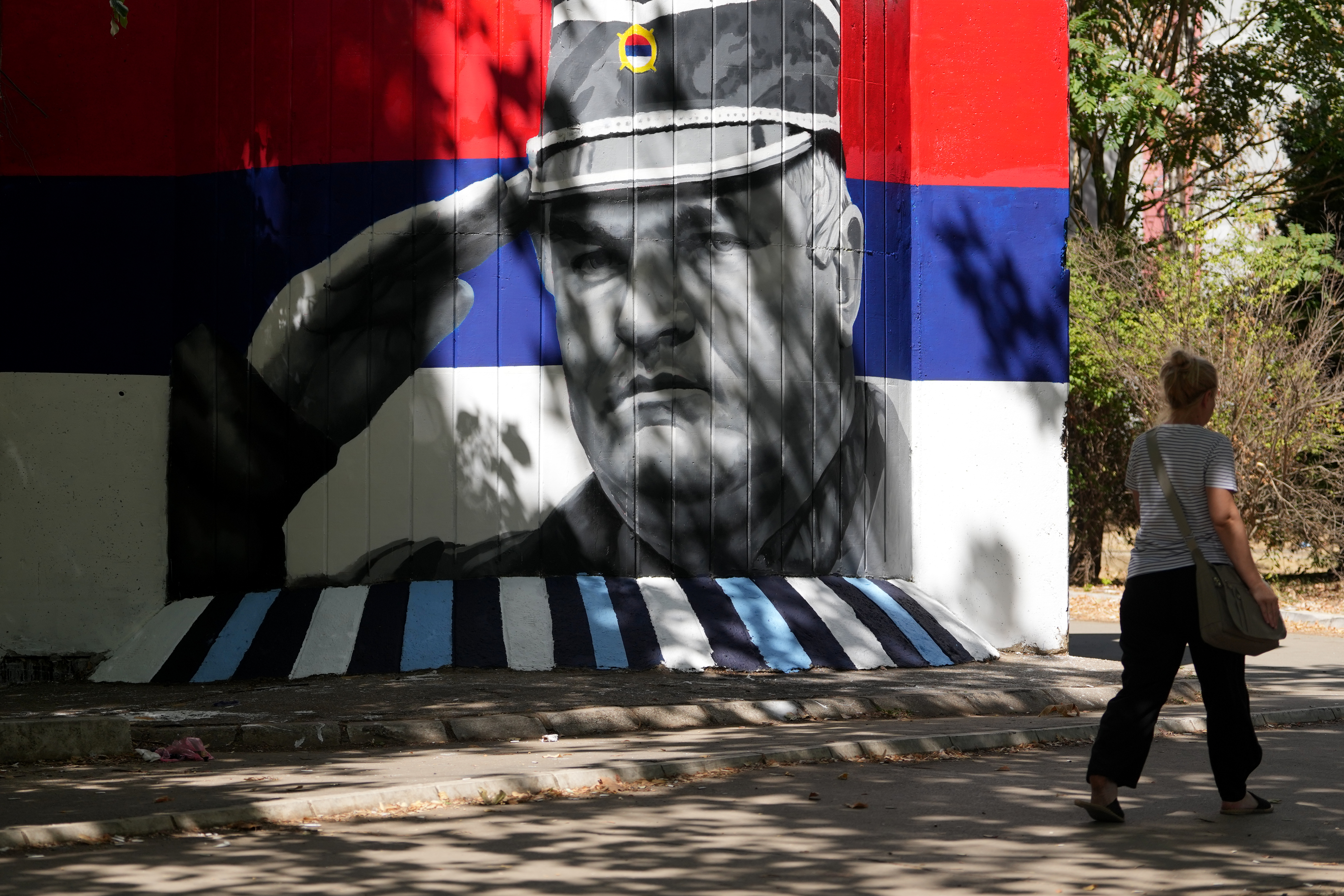 A woman walks by a mural that shows former Bosnian Serb wartime general Ratko Mladic in Belgrade. [Darko Vojinovic/AP Photo]