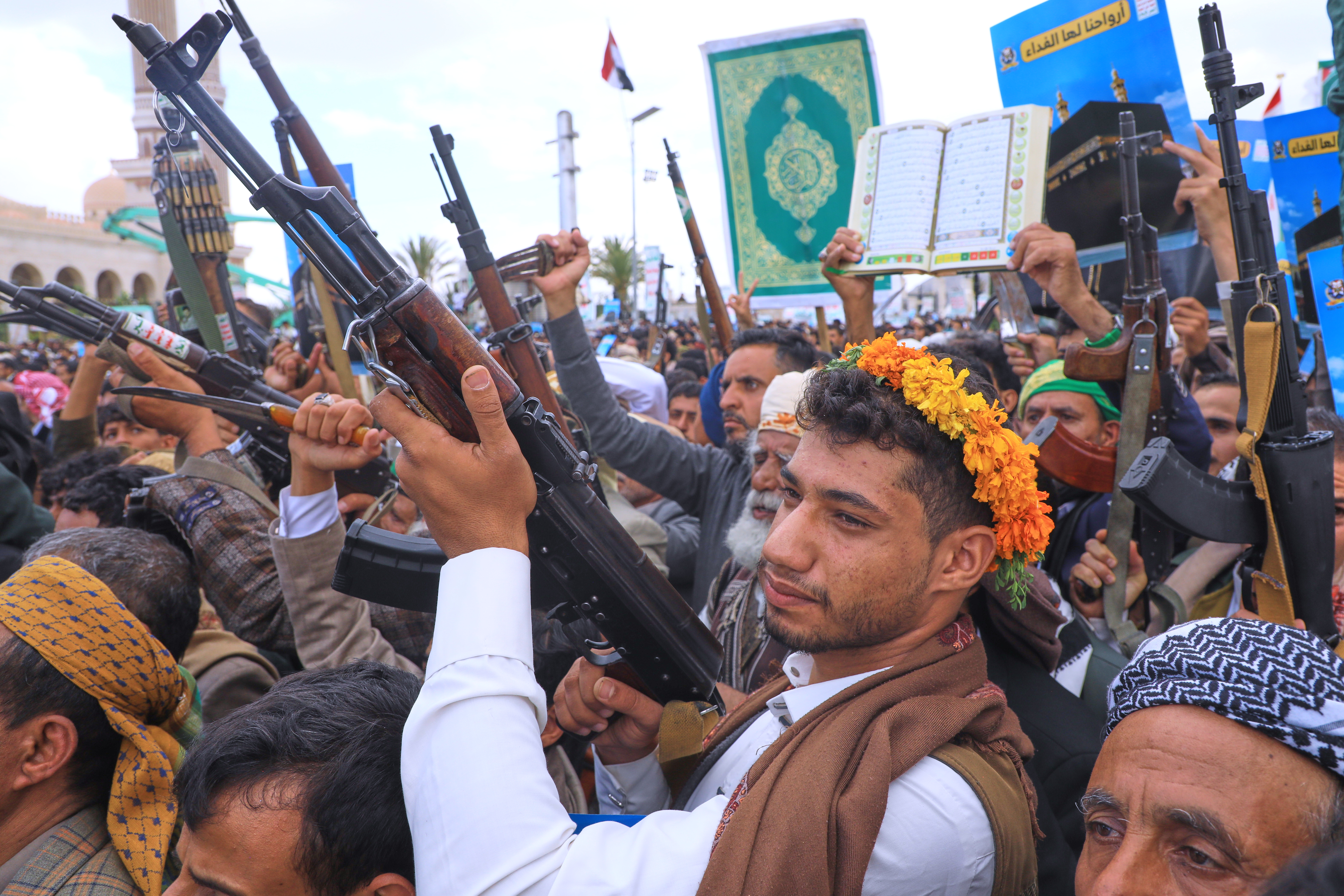A group of men raise their machineguns and one holds up a large Quran.